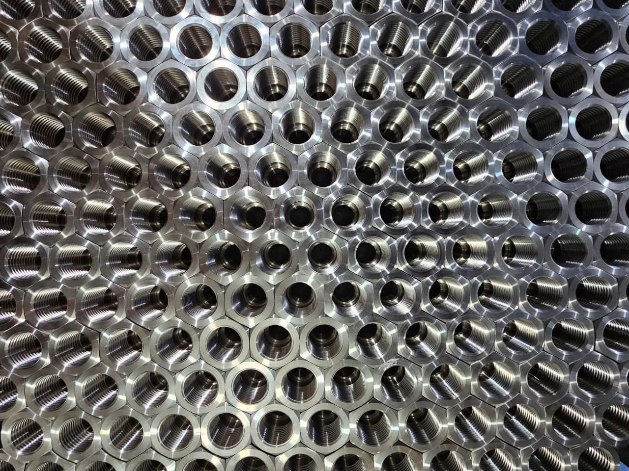 Close-up of precision-machined metal hex nuts with internal threads, arranged in rows.
