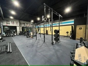 Empty gym with fitness equipment including pull-up bars, weight plates, benches, and barbells in a spacious workout area