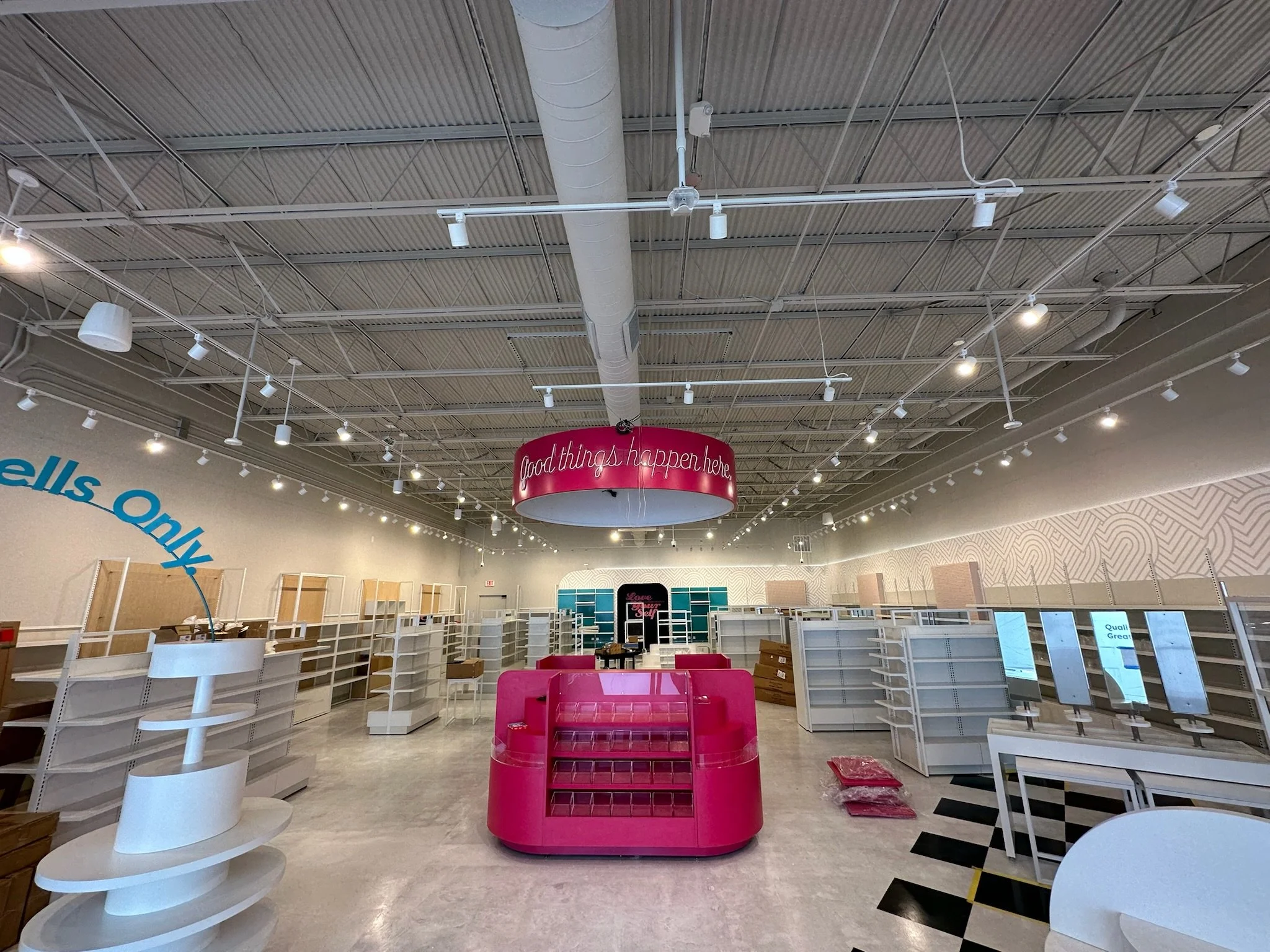 Empty retail space with missing shelves, pink display counters, and a curved pink sign overhead that reads 'Good things happen here'.