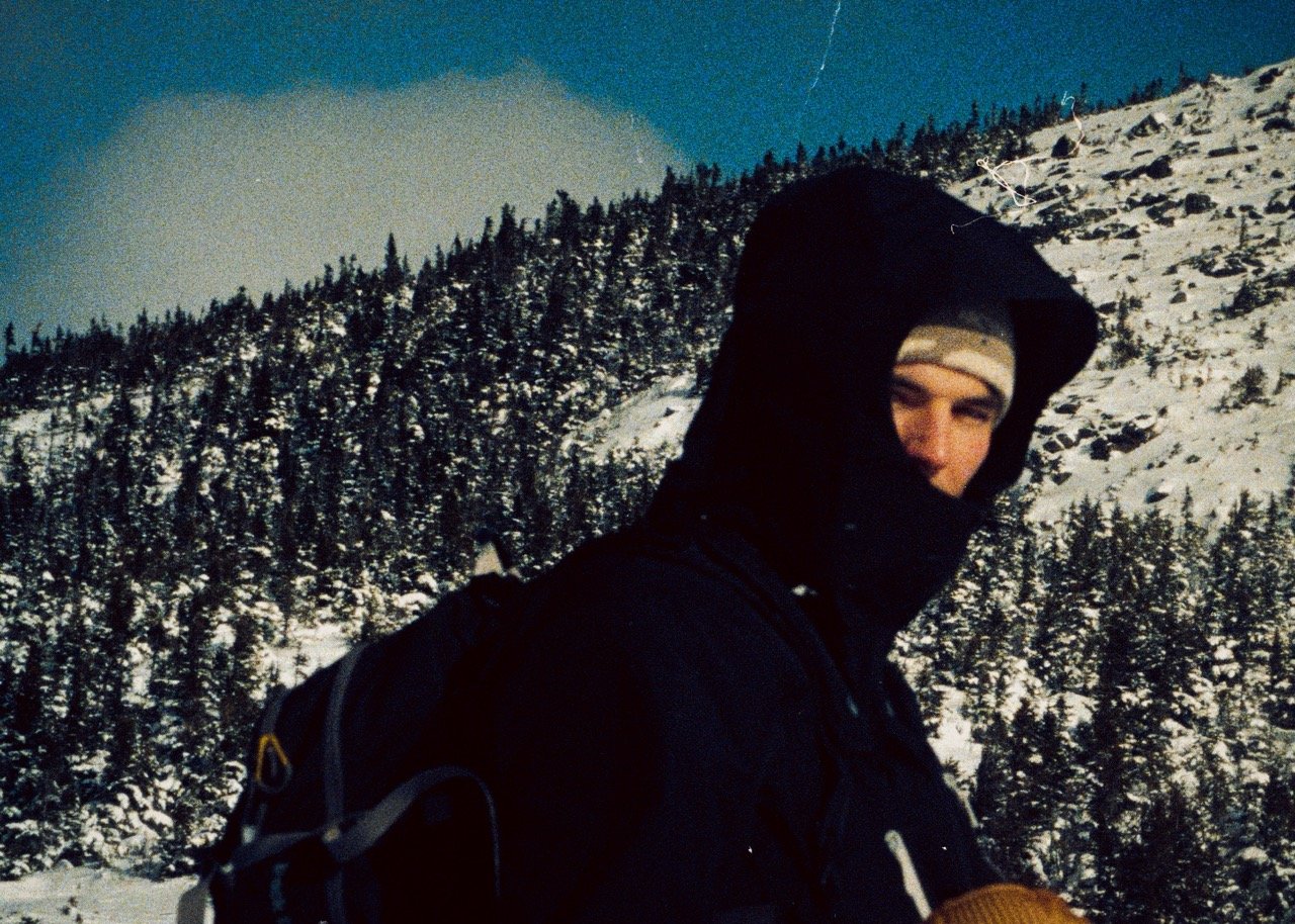 35mm Film Photo of Skier looking back at camera with trees and snowy mountain in background