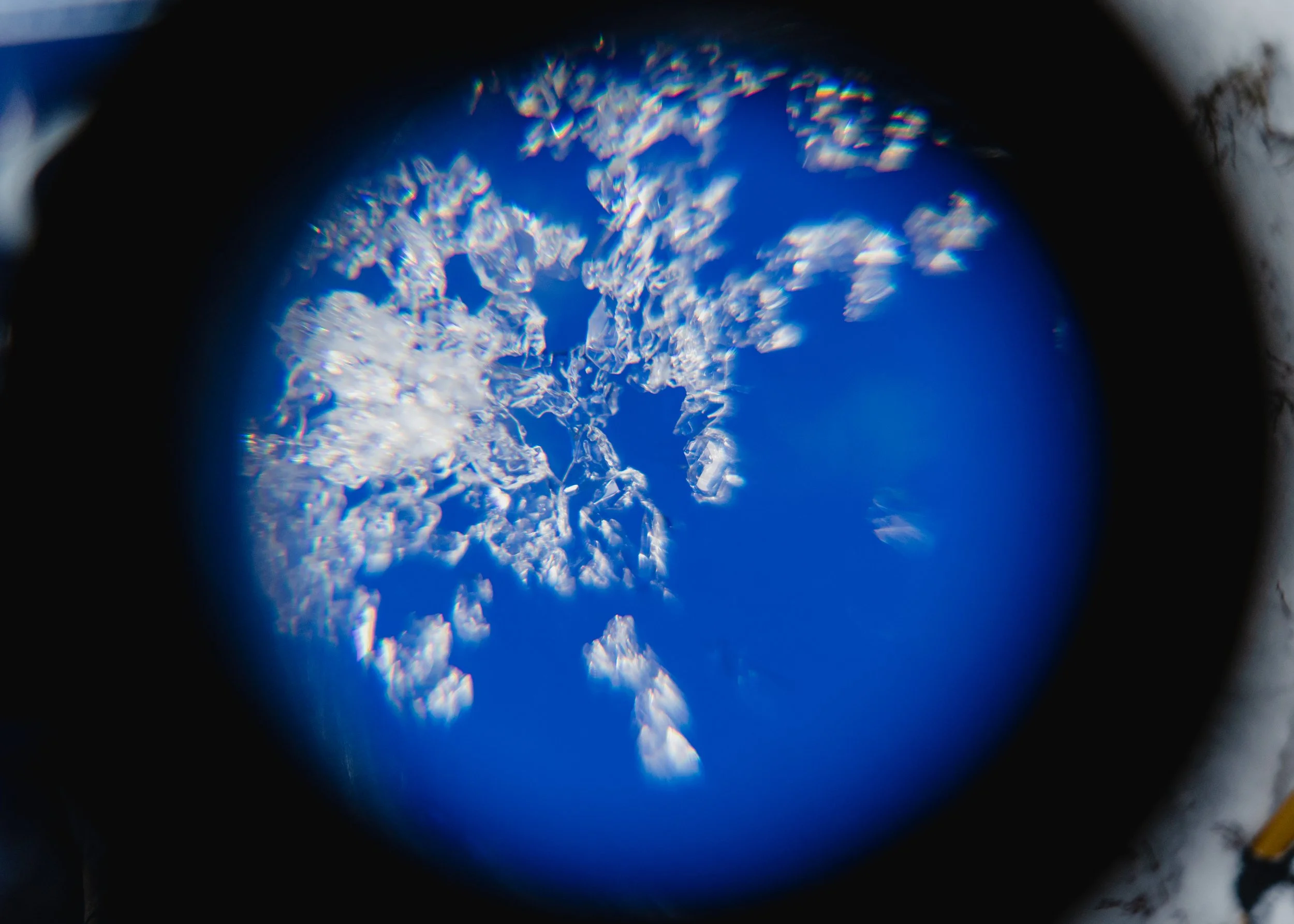 Close-up view of sparkling ice crystals on a blue surface, seen through a circular frame.
