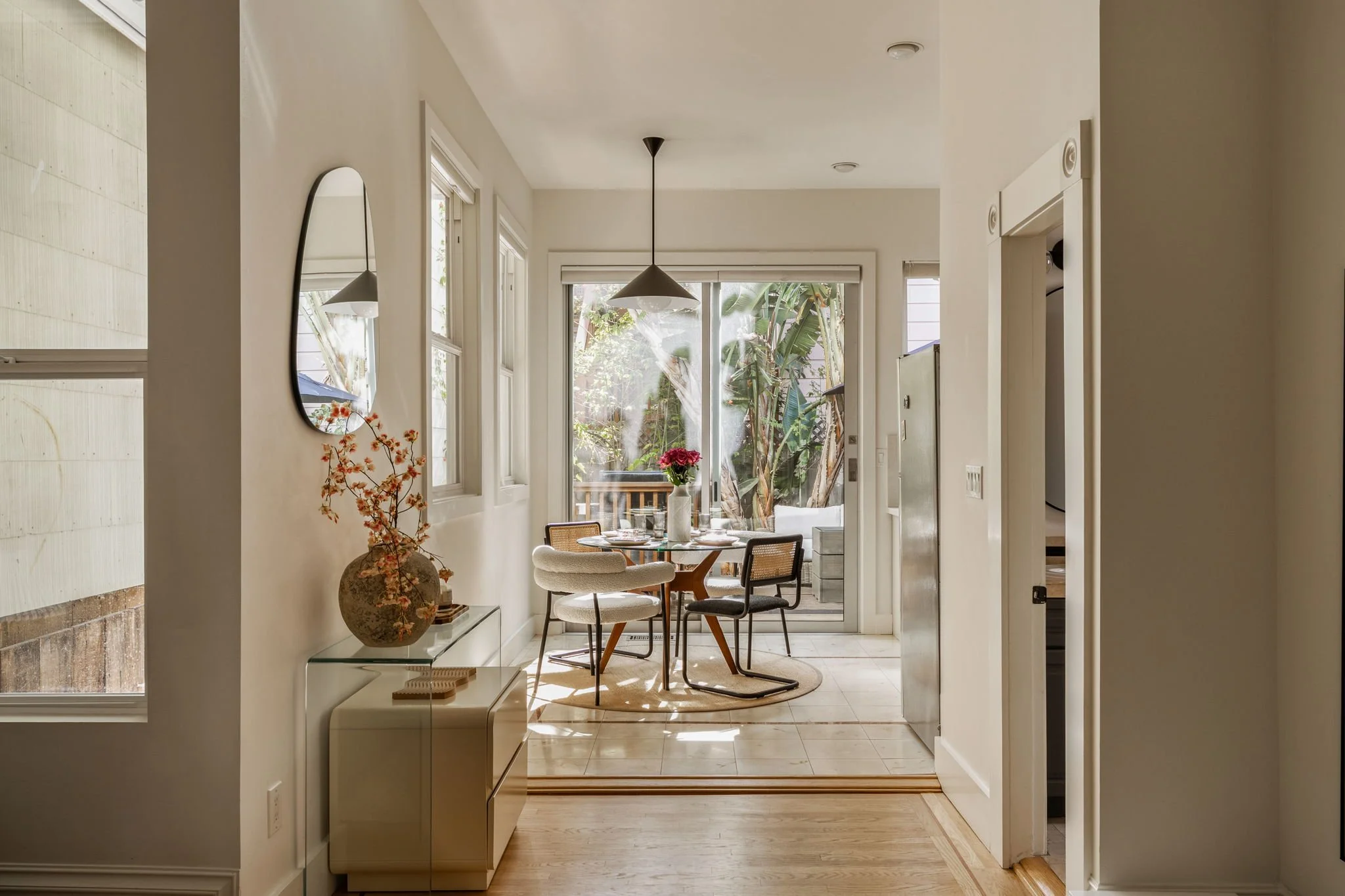 A bright dining area with a round table and four chairs, set with tableware, facing large glass doors with views of lush greenery outside.