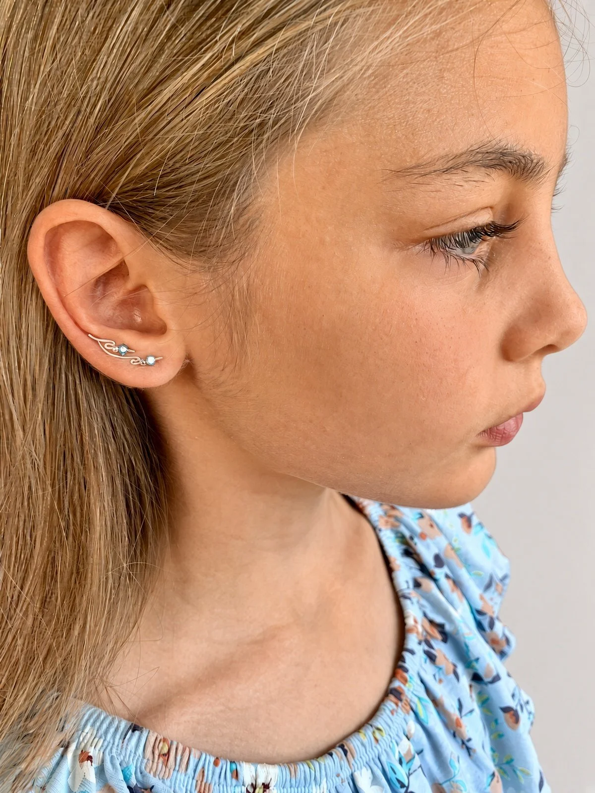 Close-up side profile of a woman wearing a blue floral top and silver ear climber earrings.