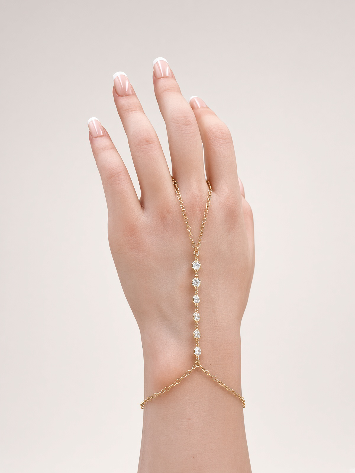 Hand wearing a delicate gold hand chain bracelet with round crystal stones and French manicure