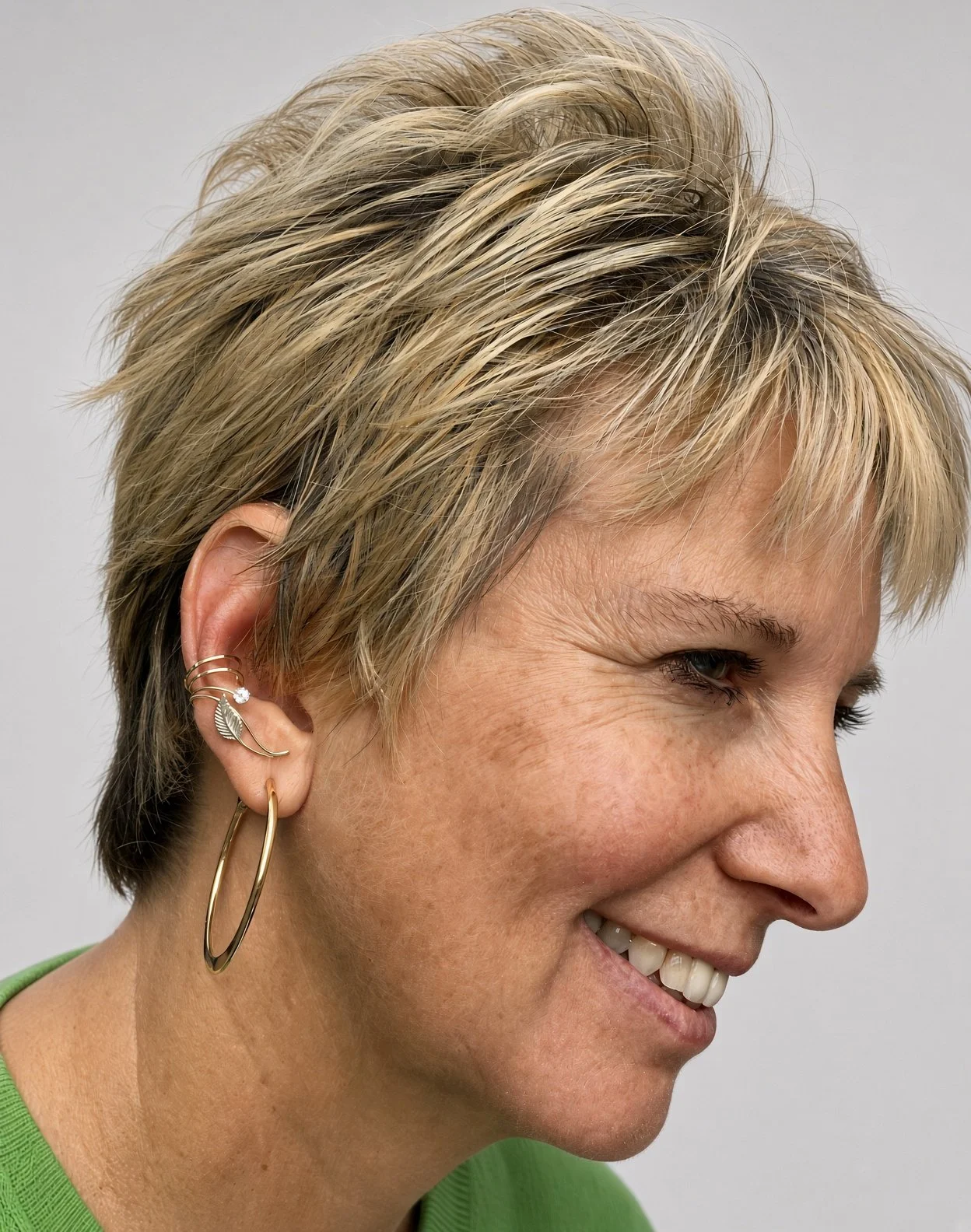 Close-up side profile of a smiling older woman with short blonde hair, gold hoop earrings, and a green top
