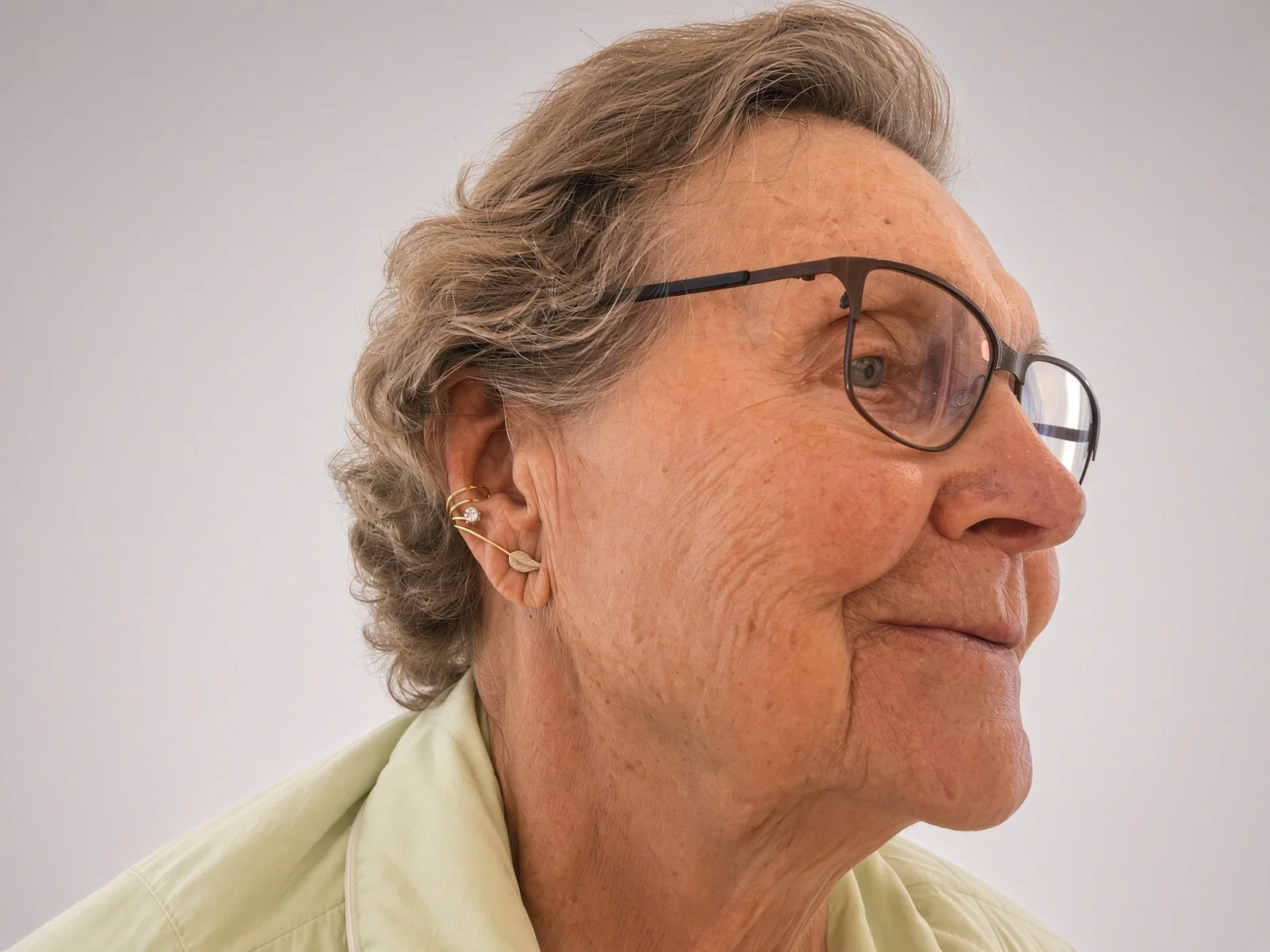 Close-up side profile of an elderly woman wearing eyeglasses and gold earrings
