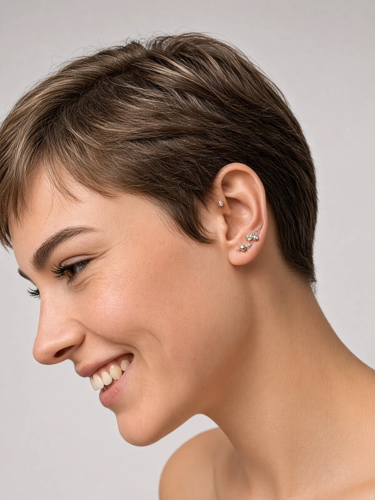 Smiling woman with short brown hair and multiple silver ear piercings