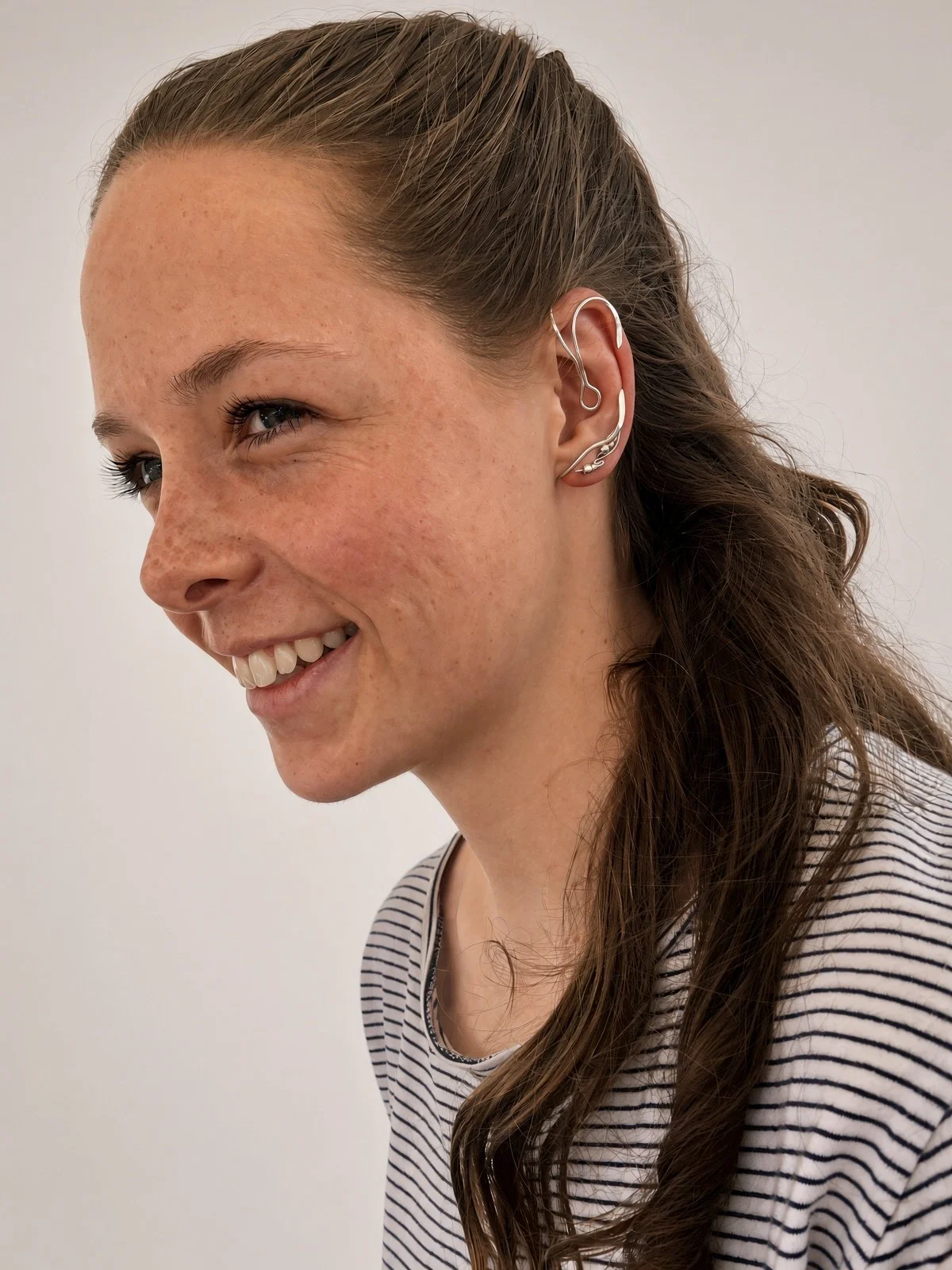 Smiling woman with long brown hair wearing multiple silver ear cuffs and earrings