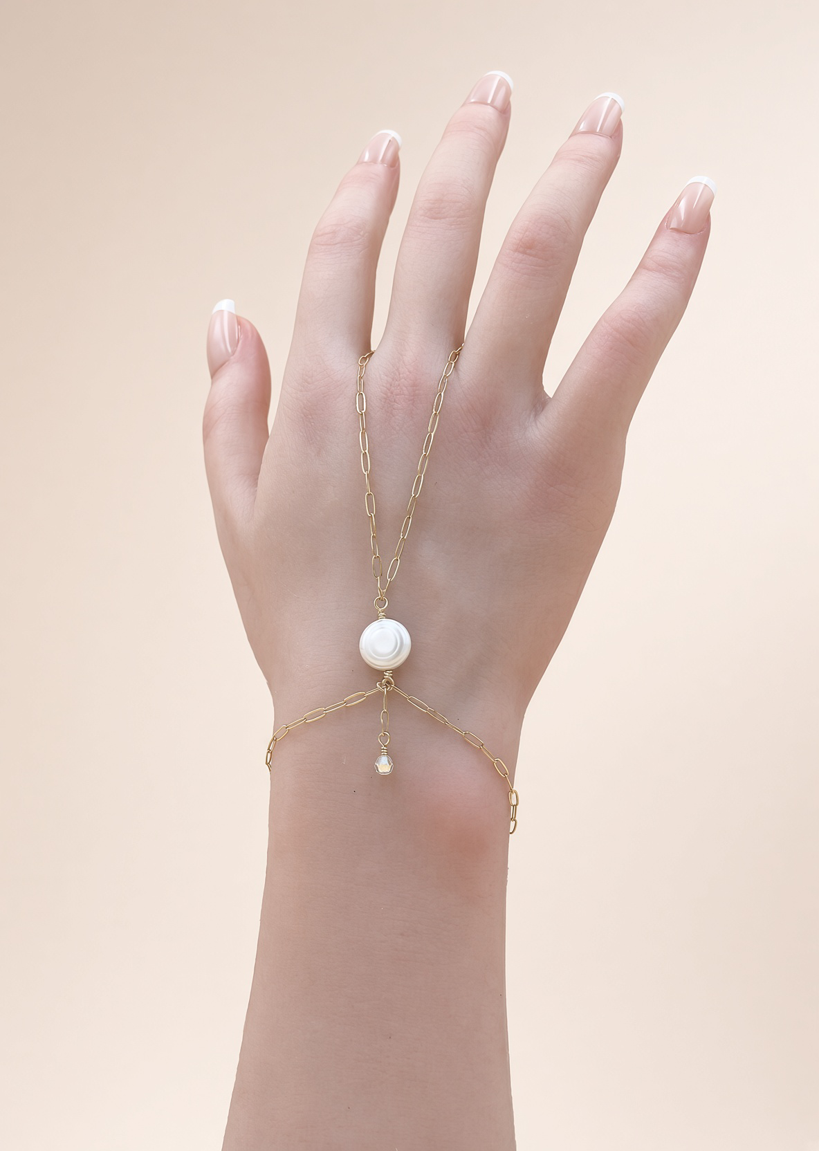 Hand wearing a delicate gold hand chain bracelet with a pearl centerpiece and dangling charm