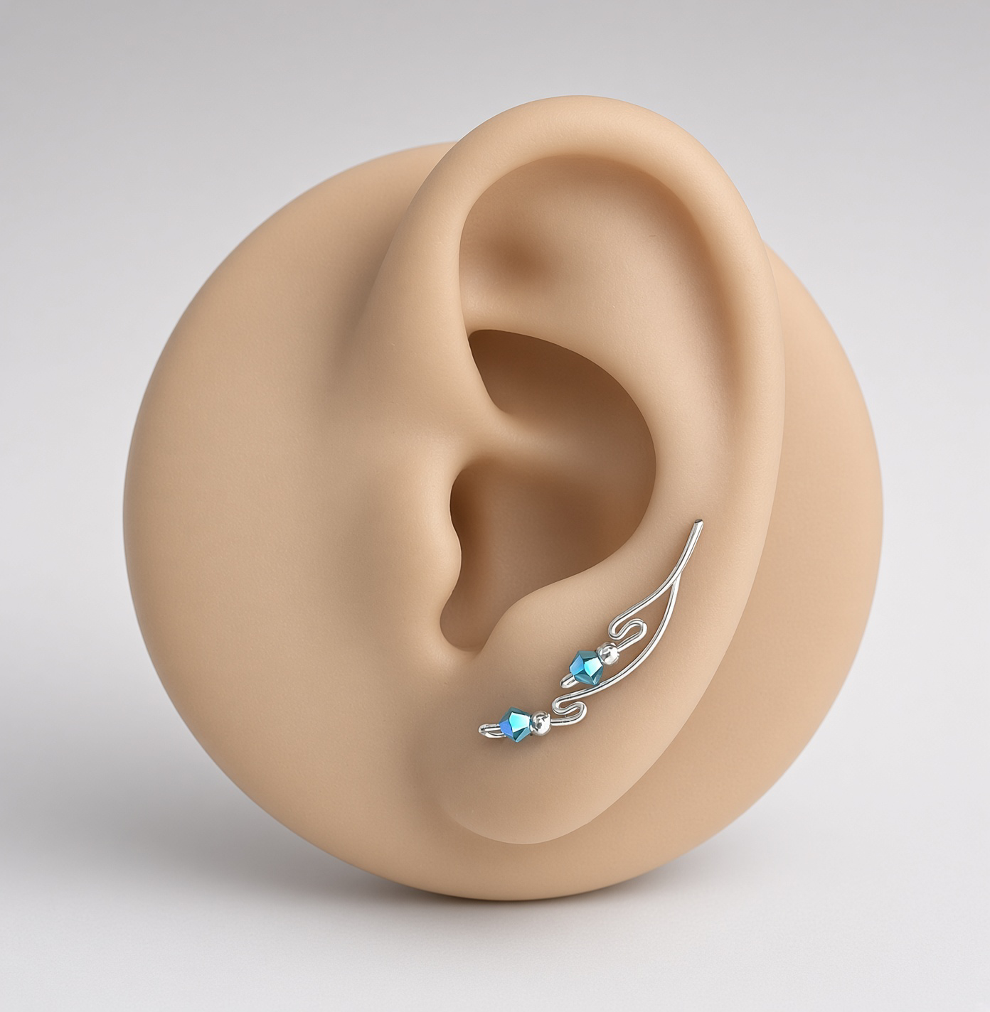 Close-up of a sculptural ear wearing a silver ear cuff with blue gemstones