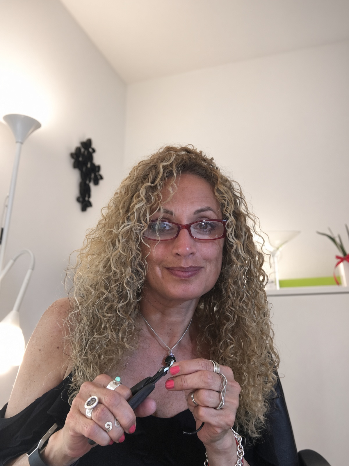 Woman with curly blonde hair and red glasses holding black hair-cutting shears indoors