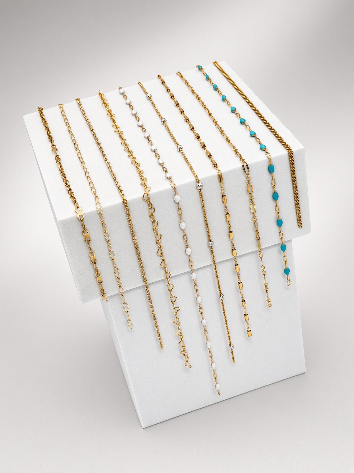 Assorted gold-tone bracelets with chain designs, white and turquoise beads displayed on a white jewelry stand
