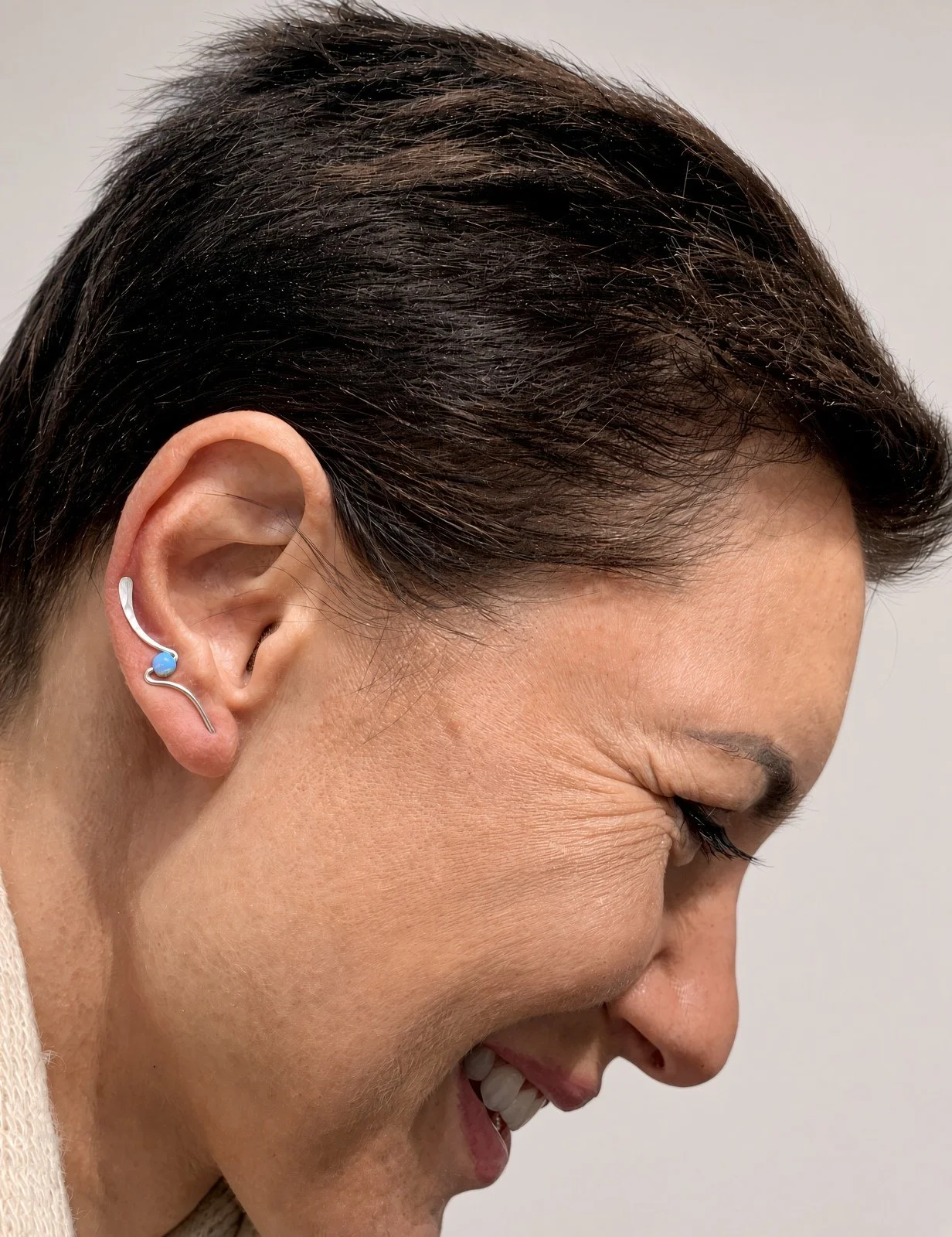 Close-up side profile of a woman with dark hair wearing a decorative ear cuff and blue gemstone earring.