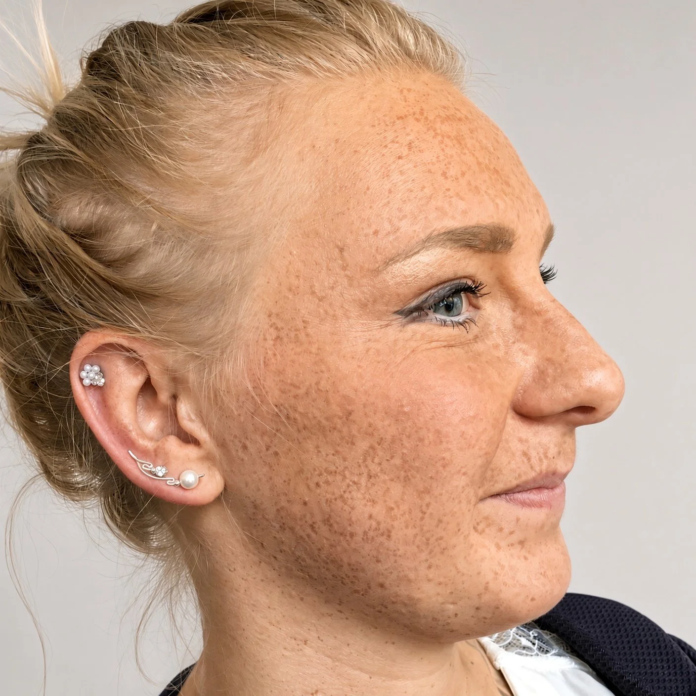 Close-up side profile of a freckled woman with blonde hair and decorative ear piercings.