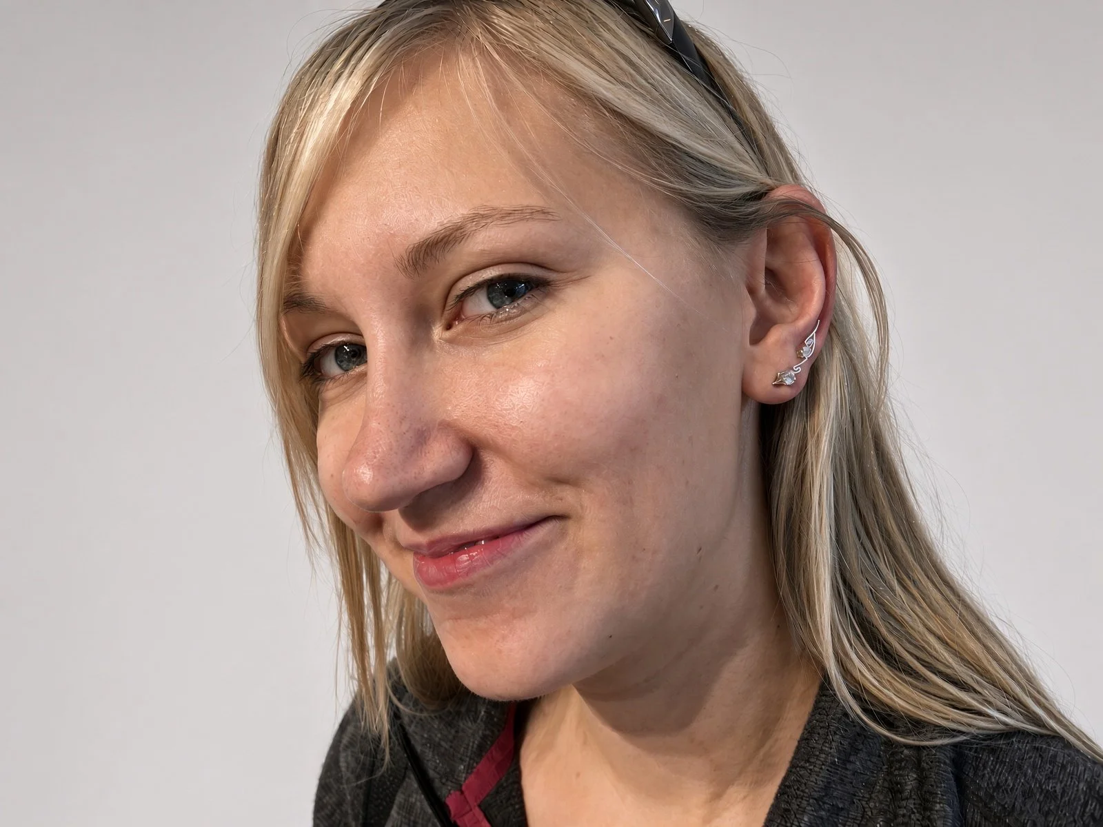 Close-up portrait of a smiling blonde woman wearing glasses on her head and silver star earrings