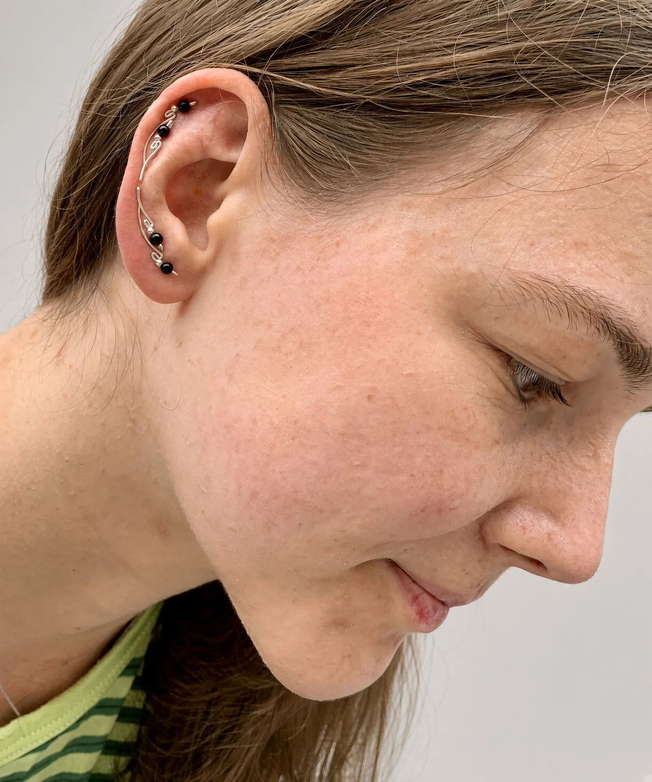 Close-up profile of a person wearing multiple black-and-silver ear piercings along the outer ear.