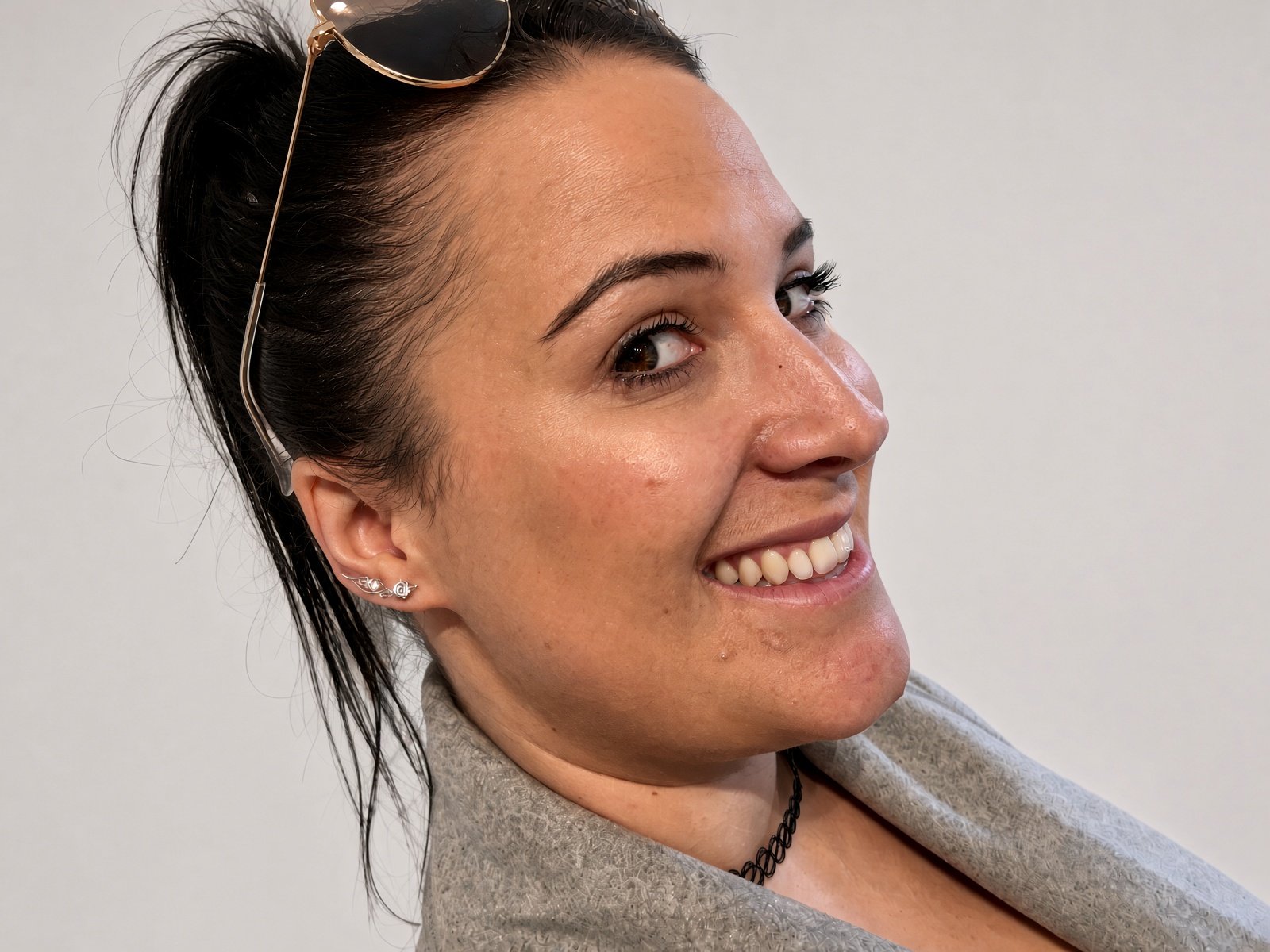 Smiling woman in side profile wearing sunglasses on her head and a gray scarf