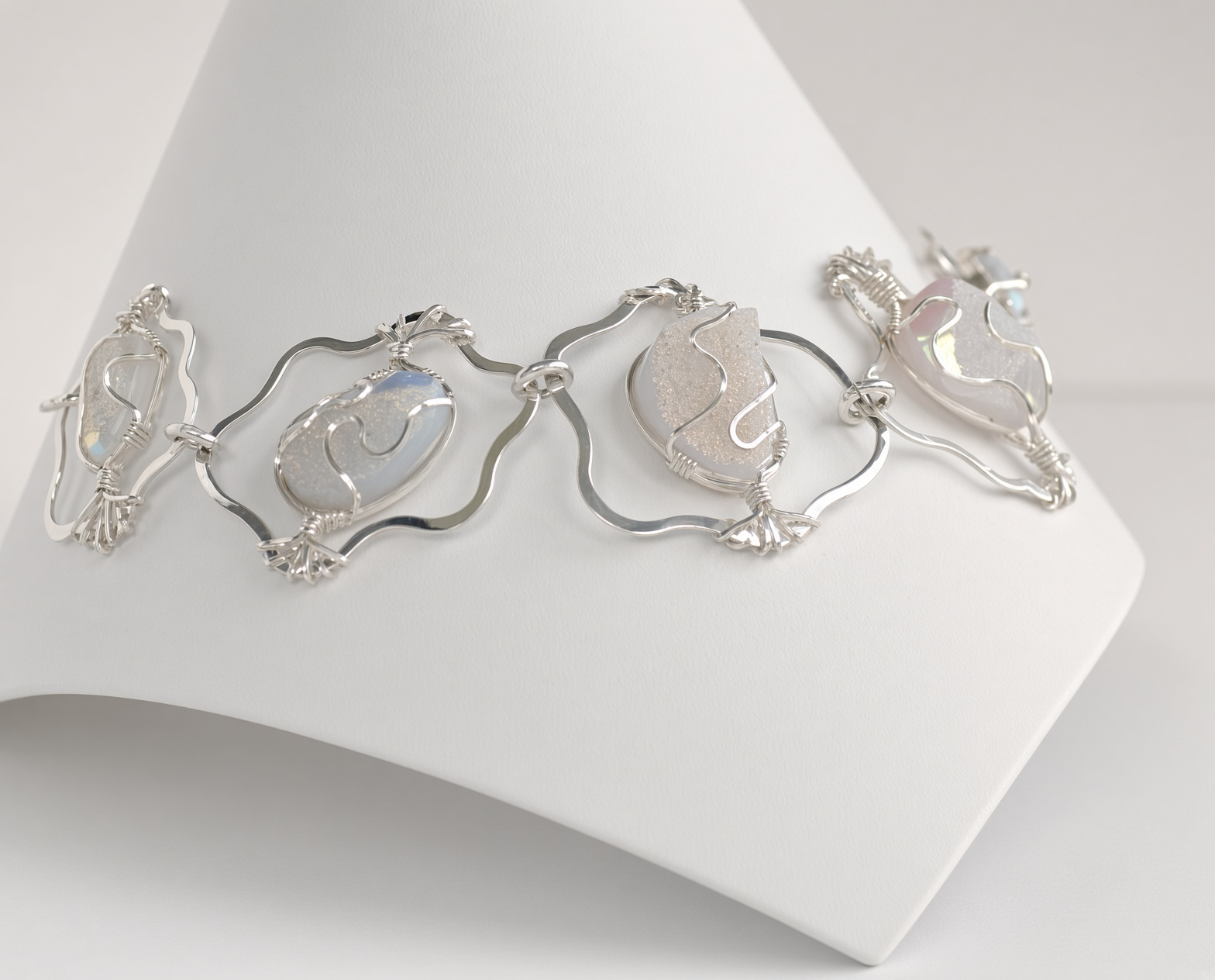 Handcrafted silver jewelry with translucent white oval gemstones displayed on a white jewelry stand
