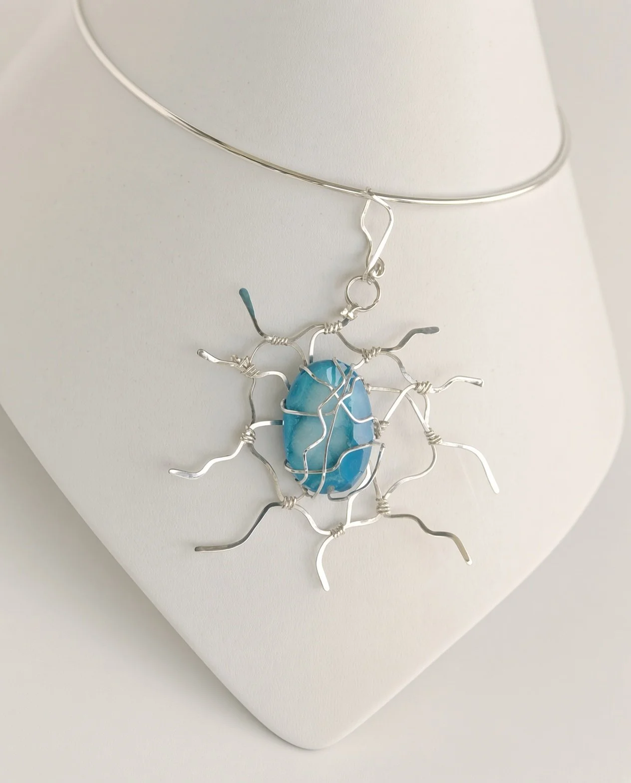 Handcrafted silver wire pendant necklace with a turquoise blue gemstone displayed on a white jewelry bust