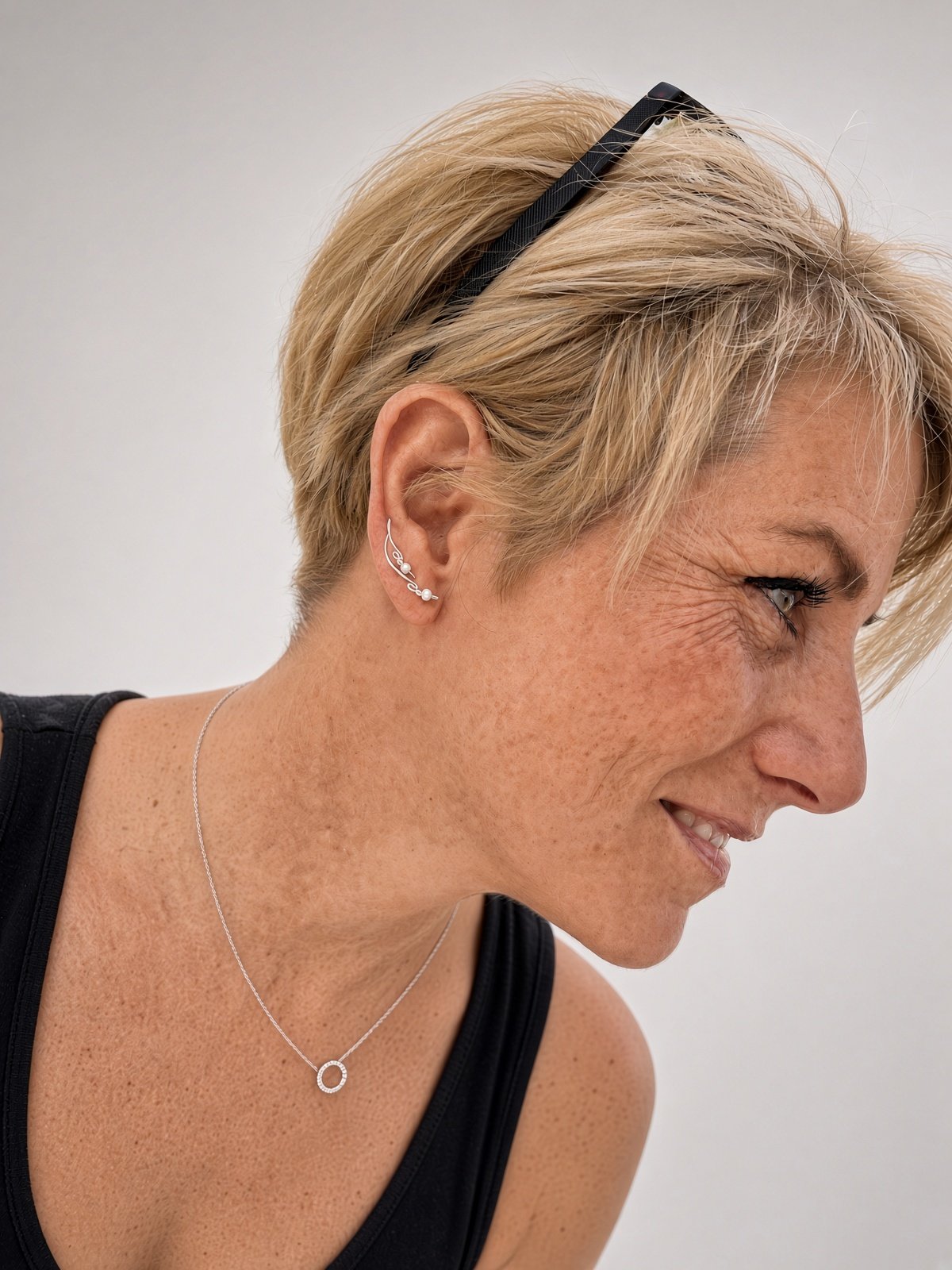 Close-up profile of a smiling older woman with short blonde hair, sunglasses on her head, and silver jewelry