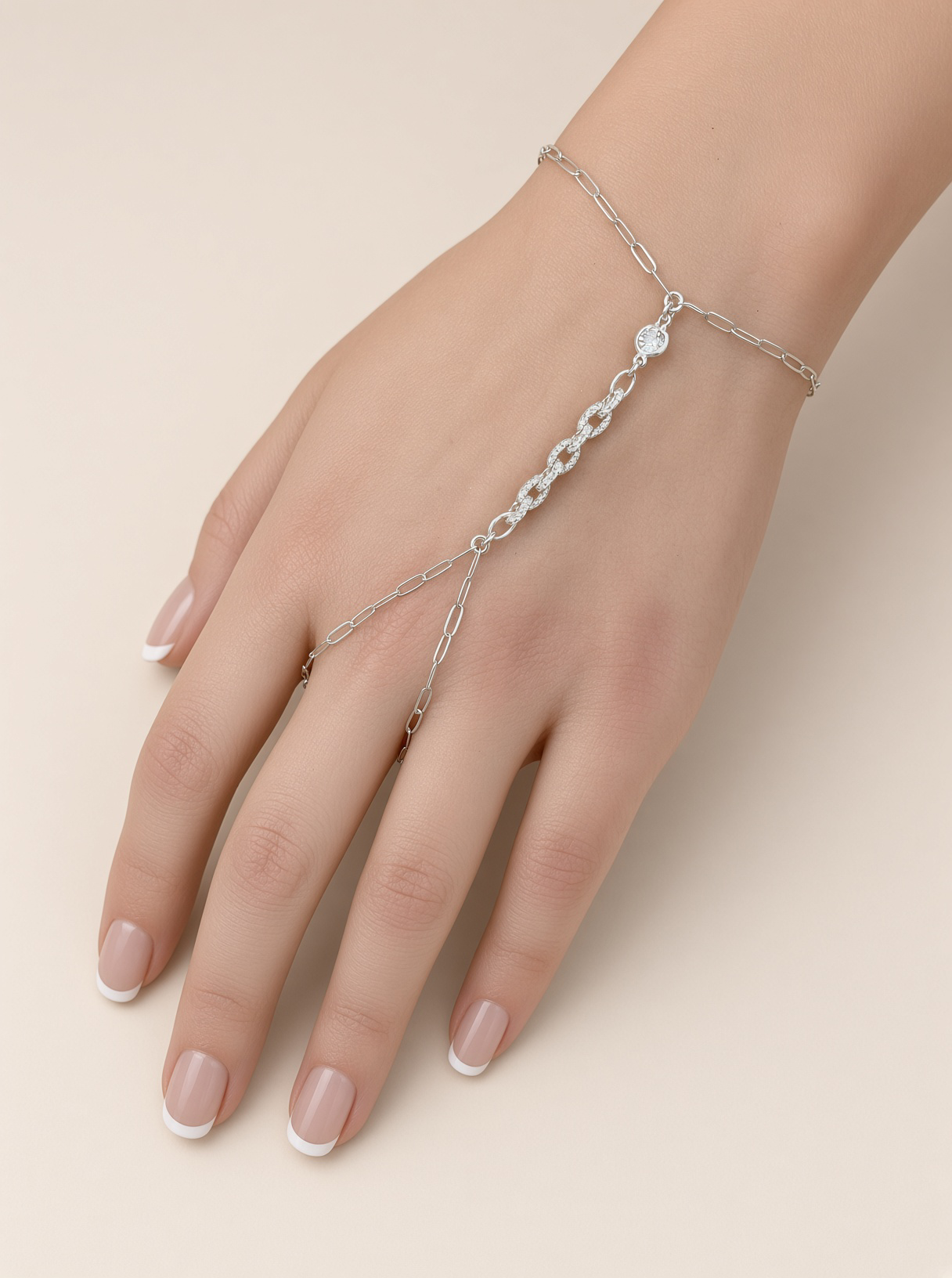 Close-up of a hand wearing a delicate silver hand chain bracelet with rhinestone accents and French manicure