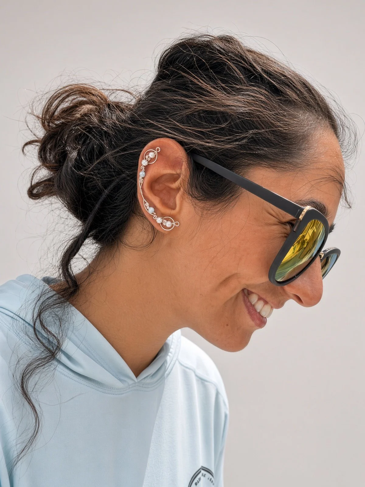 Side profile of a smiling woman wearing sunglasses and decorative ear cuff jewelry.