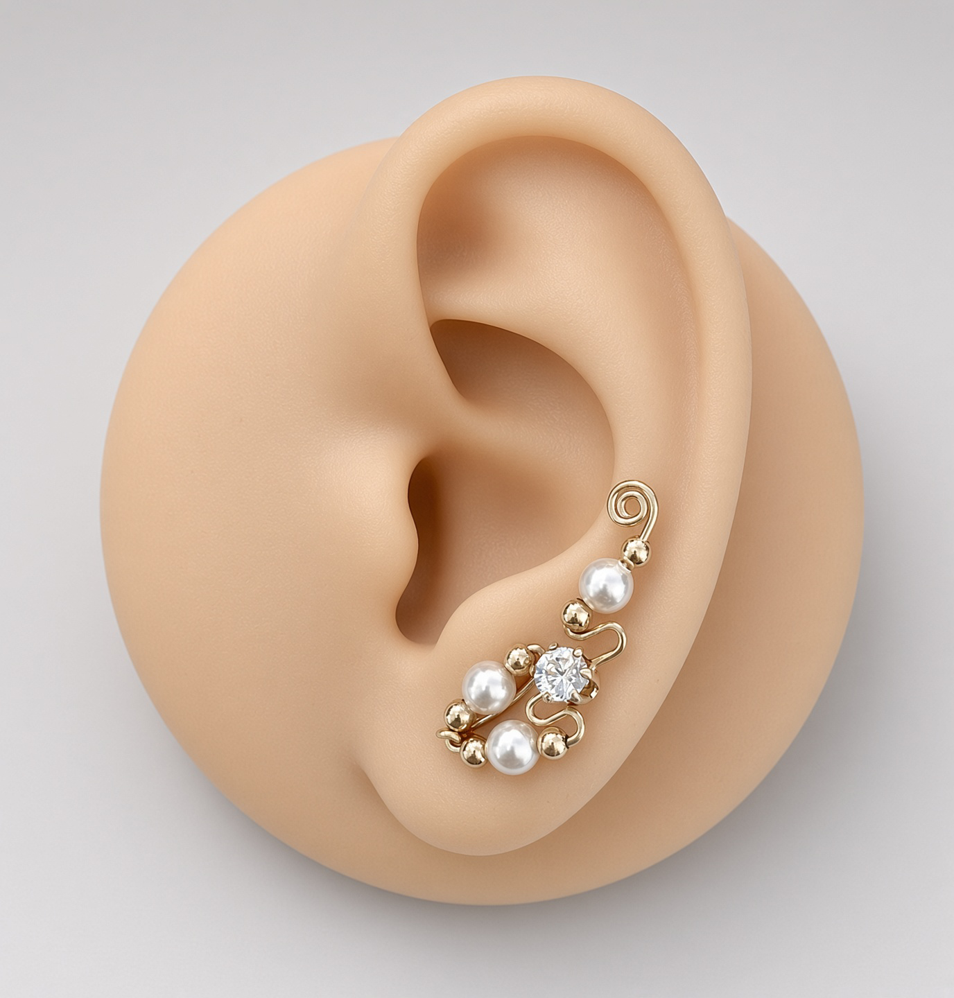 Gold ear cuff with pearls and a clear gemstone displayed on a mannequin ear