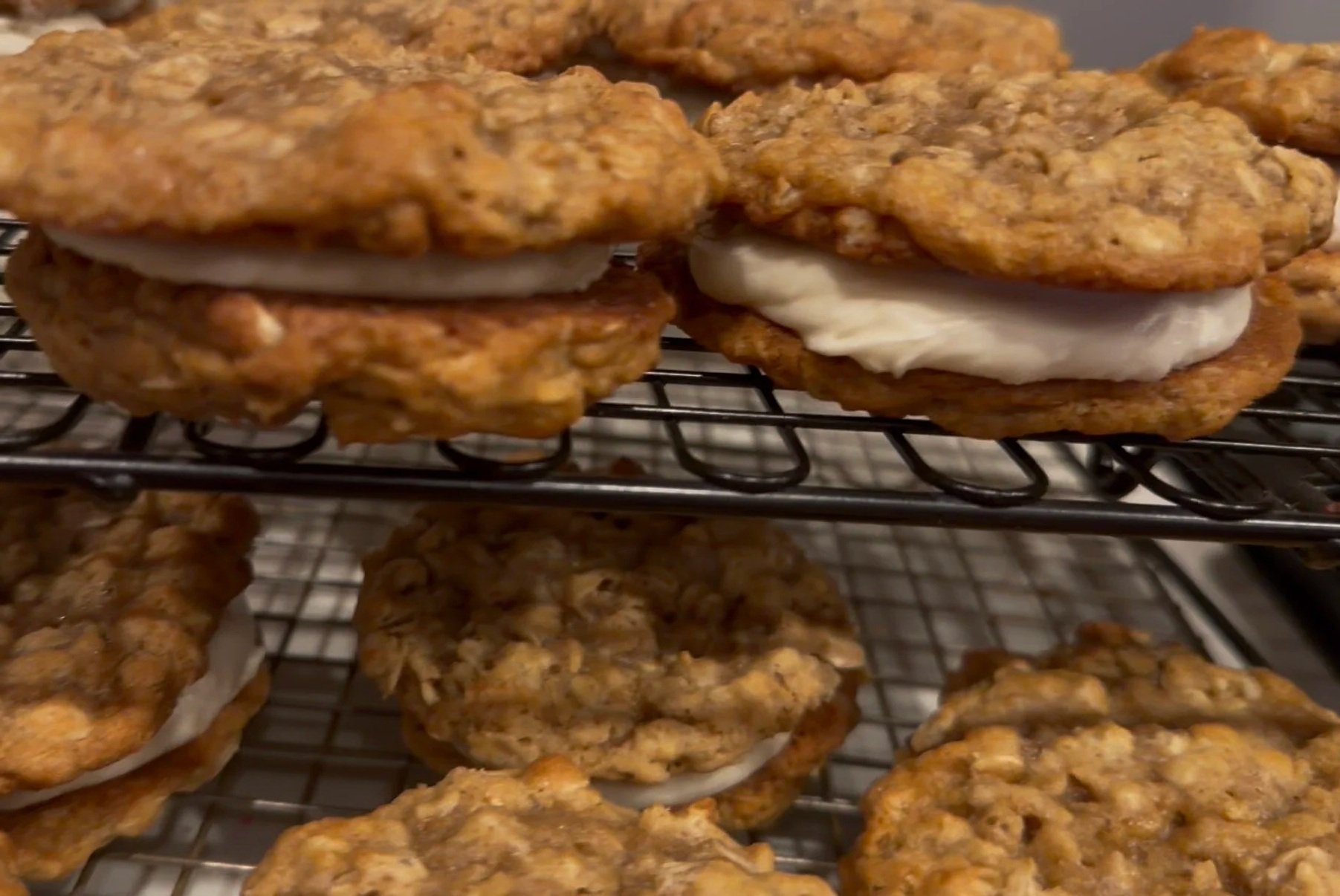 Oatmeal cookies cooling on a wire rack with some showing cream filling.
