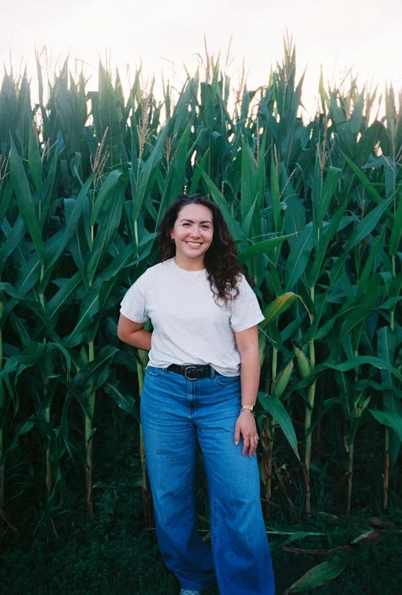 Smiling woman posing in a cornfield wearing a white T-shirt and blue jeans.