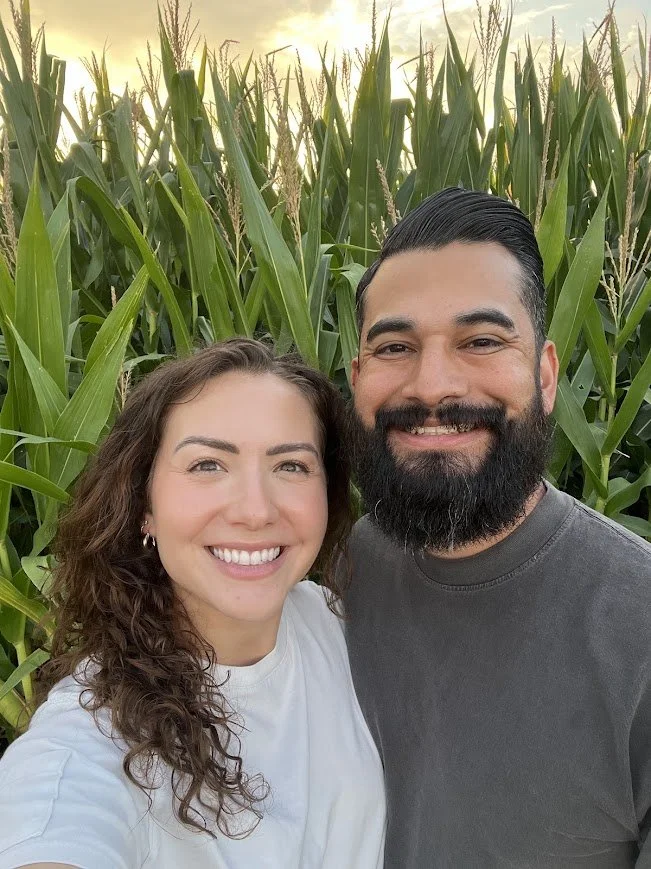 Smiling couple taking a selfie in front of a cornfield at sunset