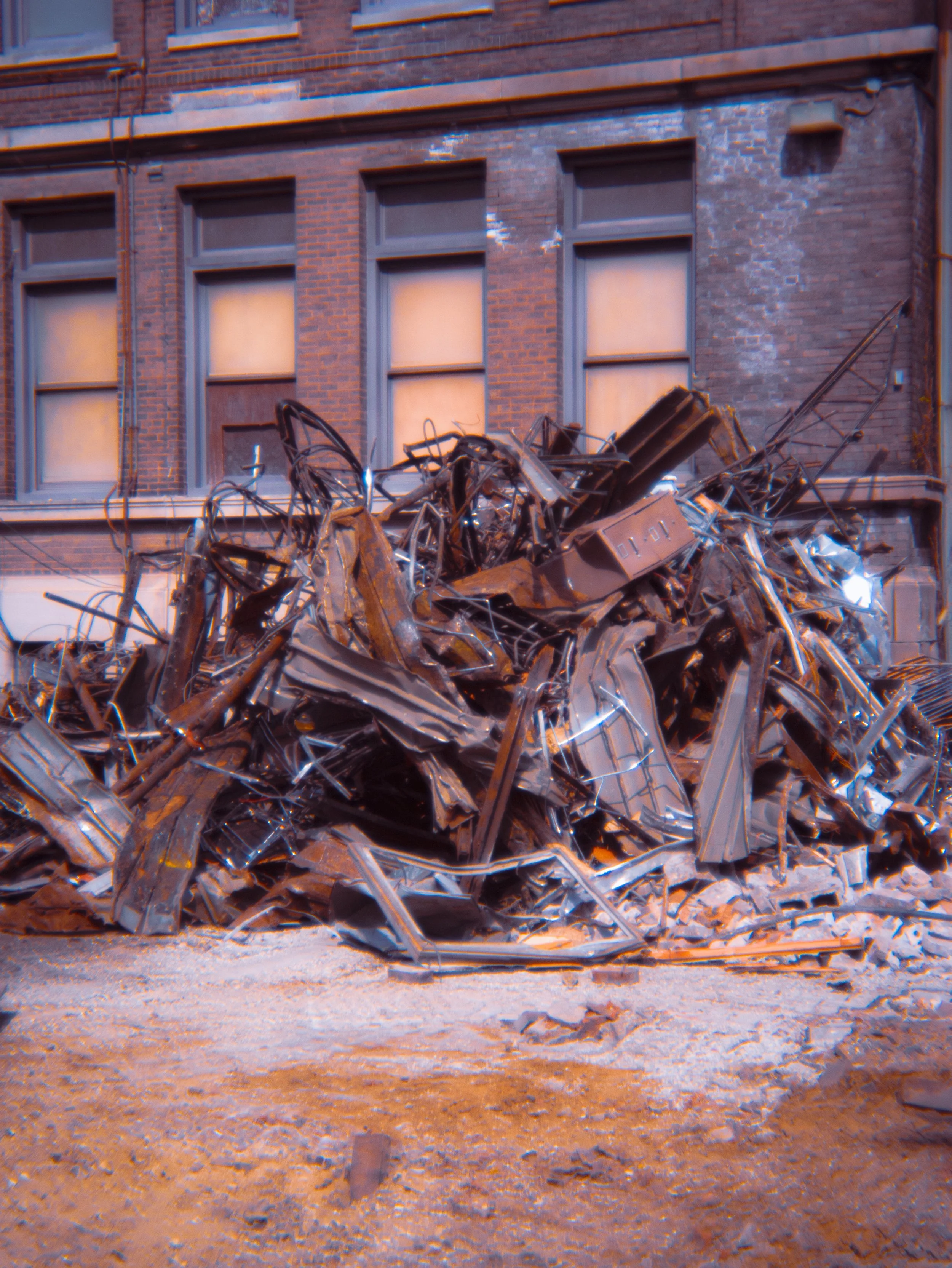 A pile of mangled and wrecked metal debris in front of a brick building with multiple windows.
