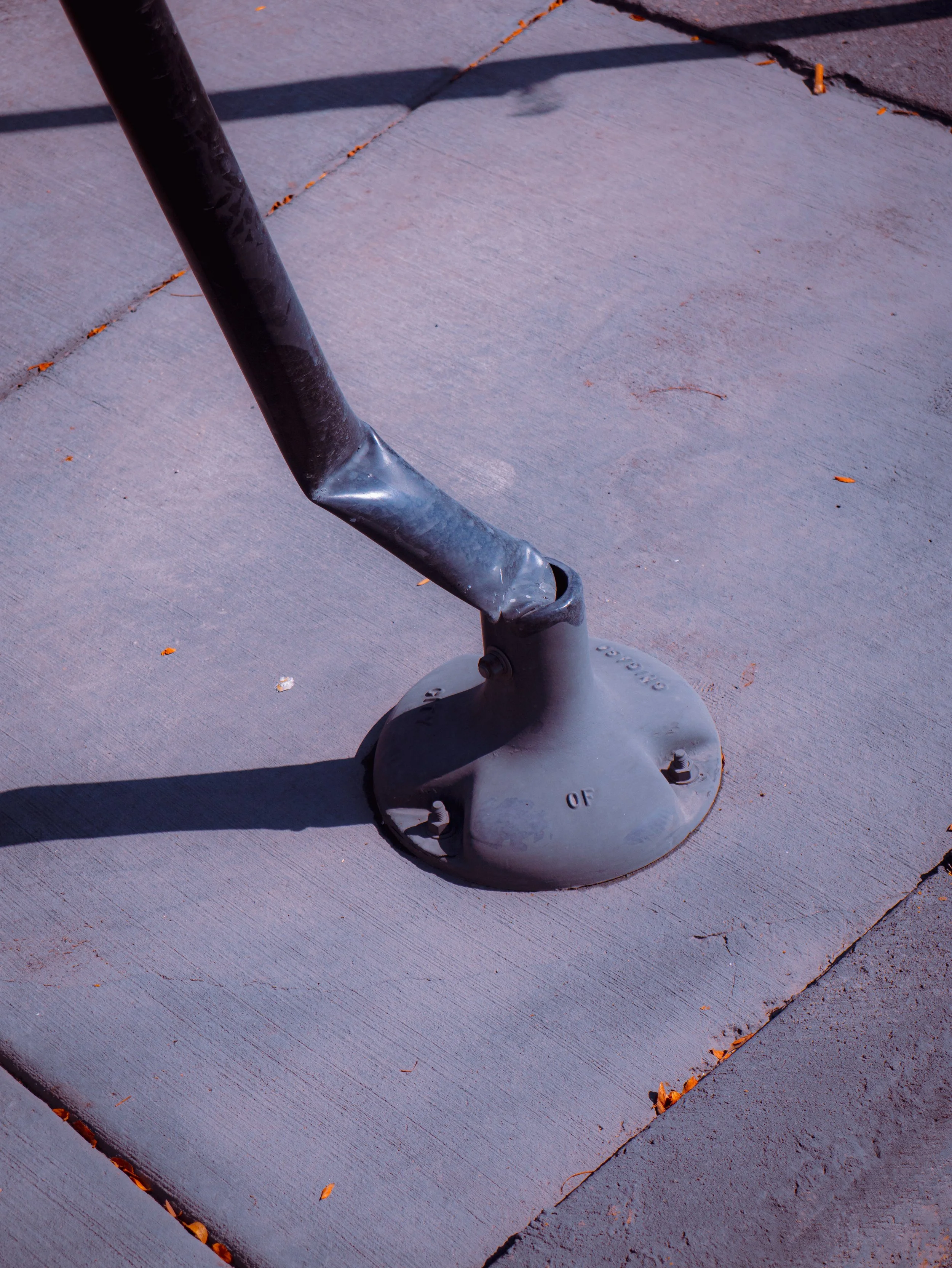Close-up of a metal bike rack on concrete sidewalk with orange-painted cracks and scattered small leaves.