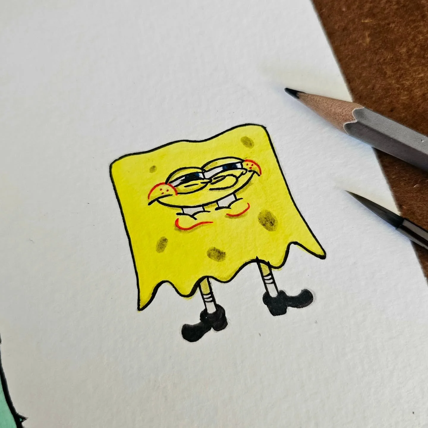 A drawing of SpongeBob SquarePants with a mischievous expression on a piece of white paper, surrounded by two pencils.