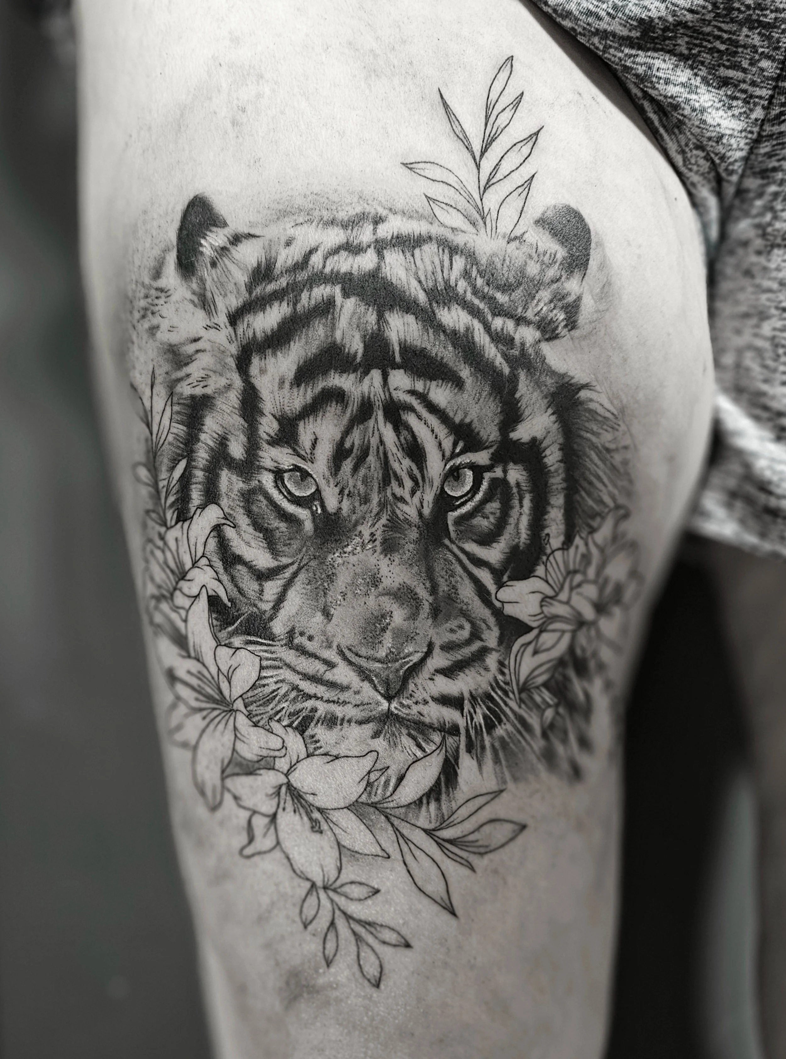 Black and white tattoo of a tiger's face surrounded by leaves on a person's skin.