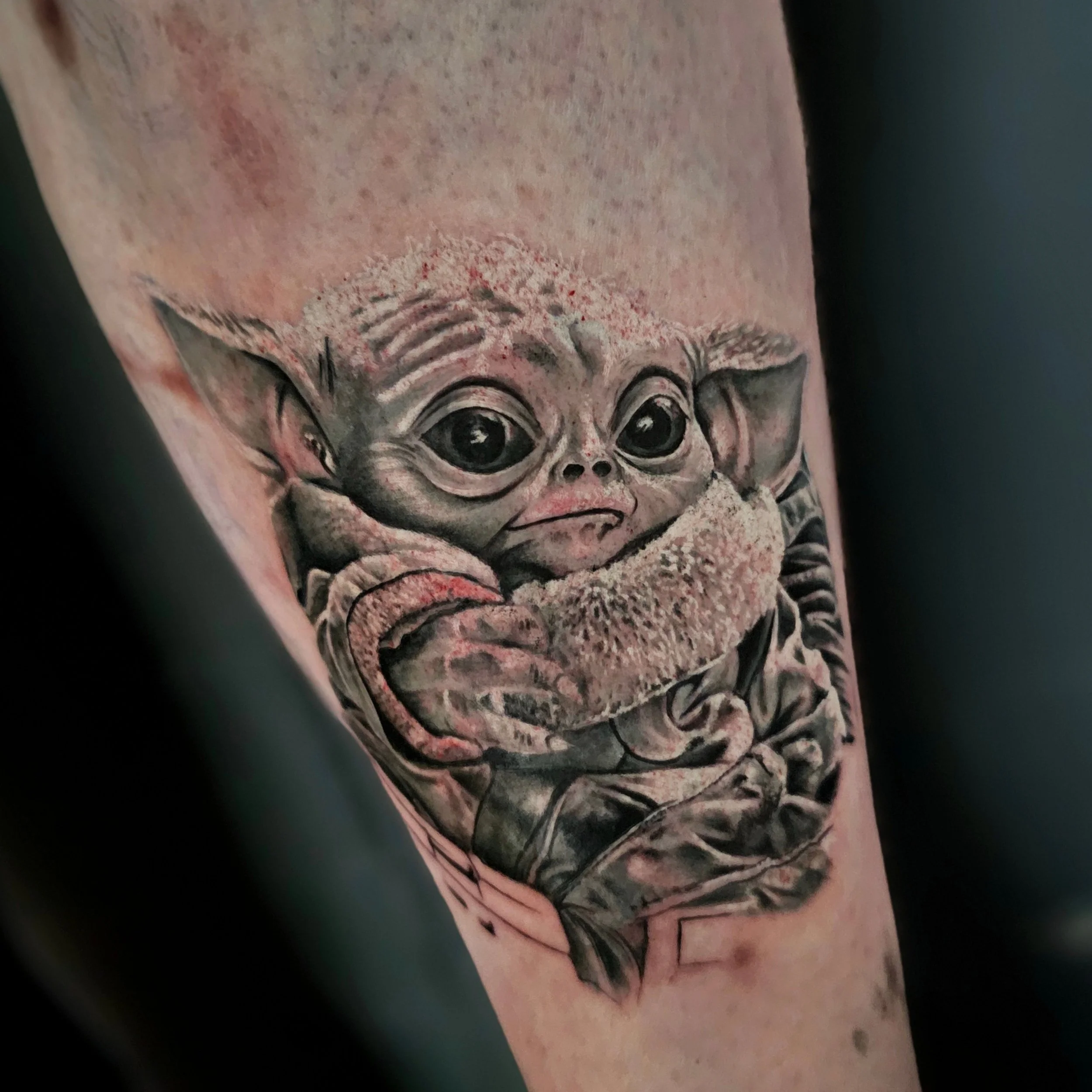 Close-up of a tattoo featuring a detailed face with large eyes, eyebrows, nose, and lips, with pinkish hues and shading on the skin.