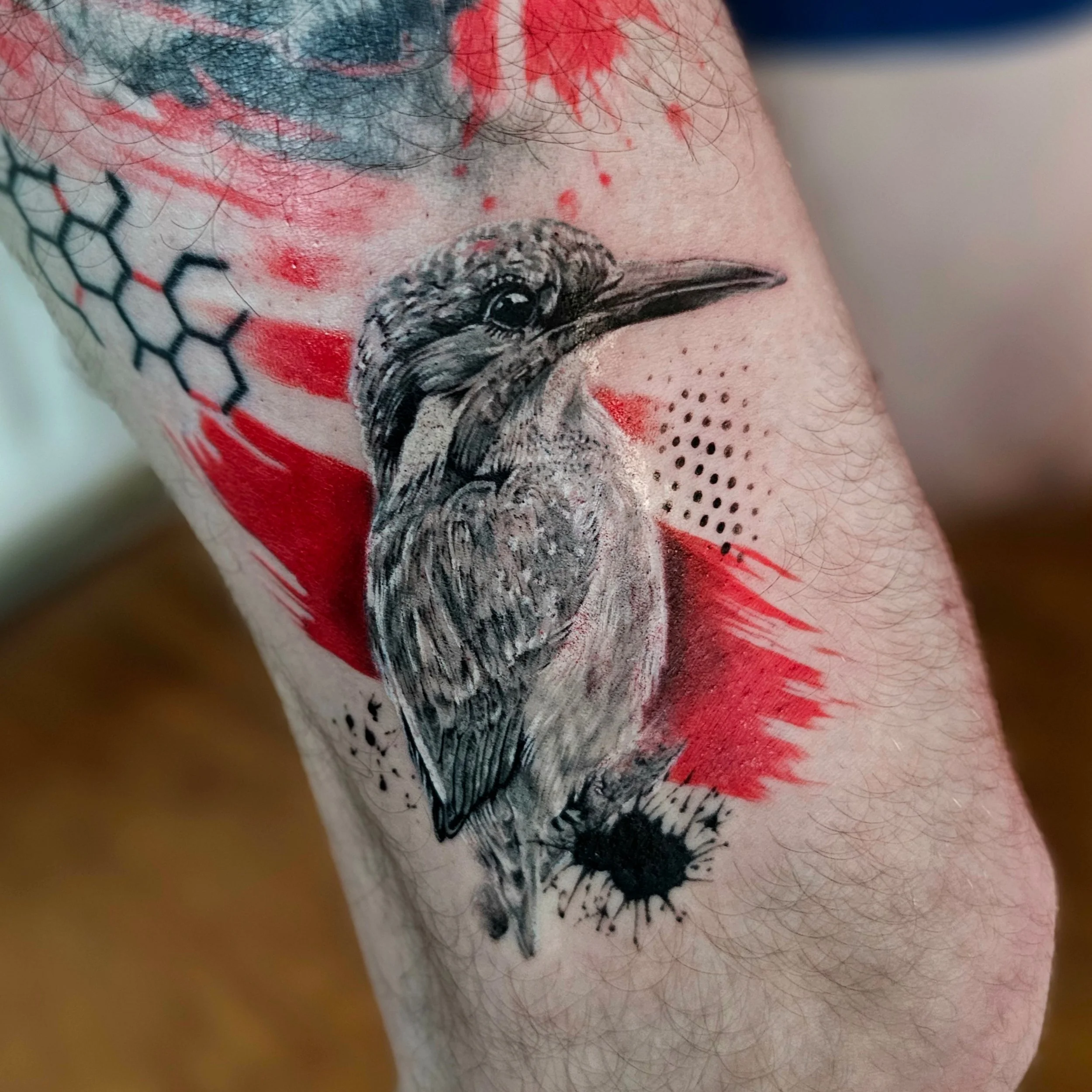 Close-up of a person's skin with a tattoo of a dog, with red, black, and blue ink, and some red markings around it.
