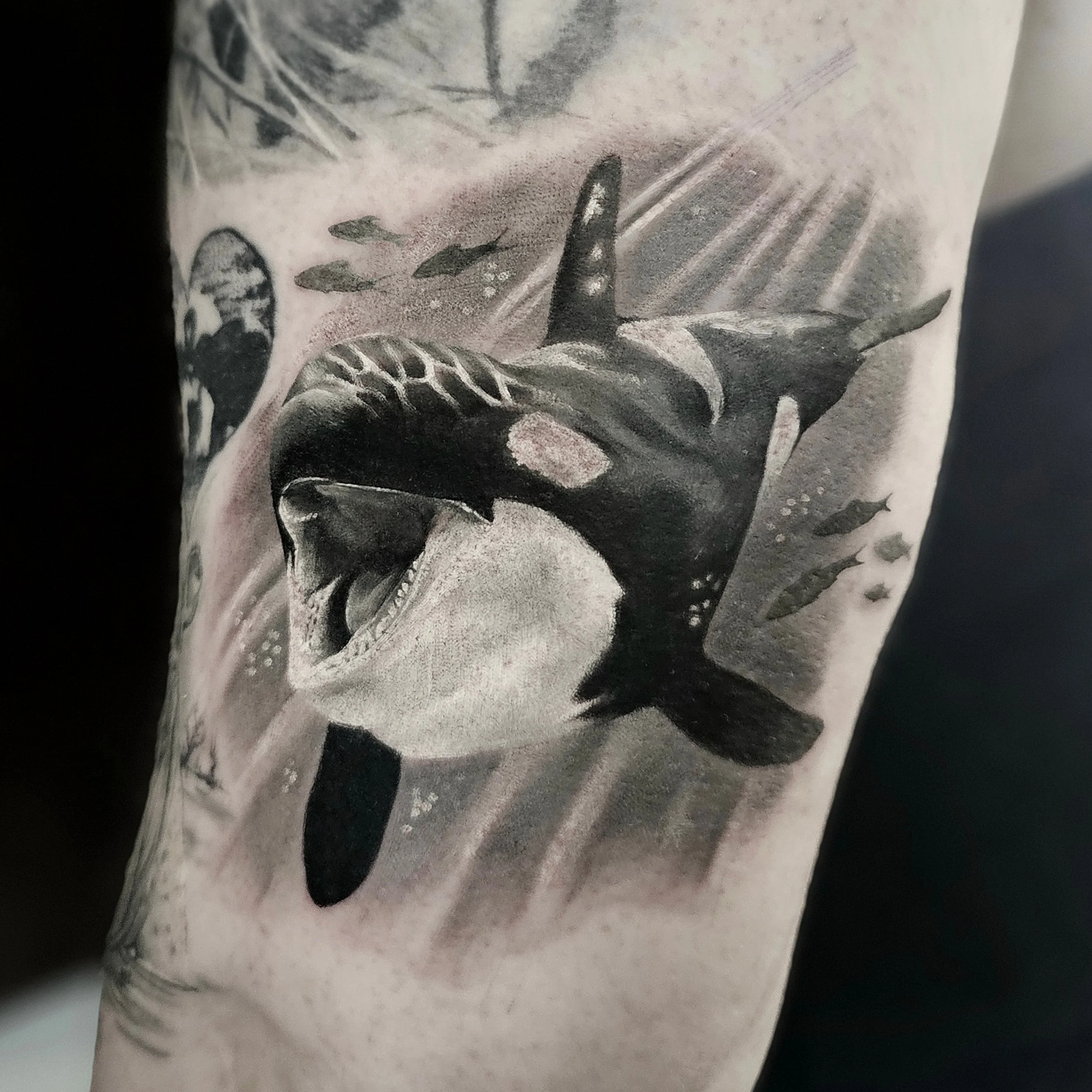 Close-up of a black and gray tattoo of a face with a dark background.
