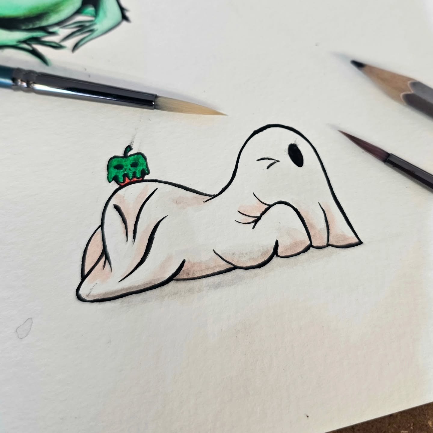 A drawing of a muscular cartoon-style woman with a black eye and long eyelashes, lying on her stomach with a green and red skull hanging from her back, surrounded by paintbrushes.