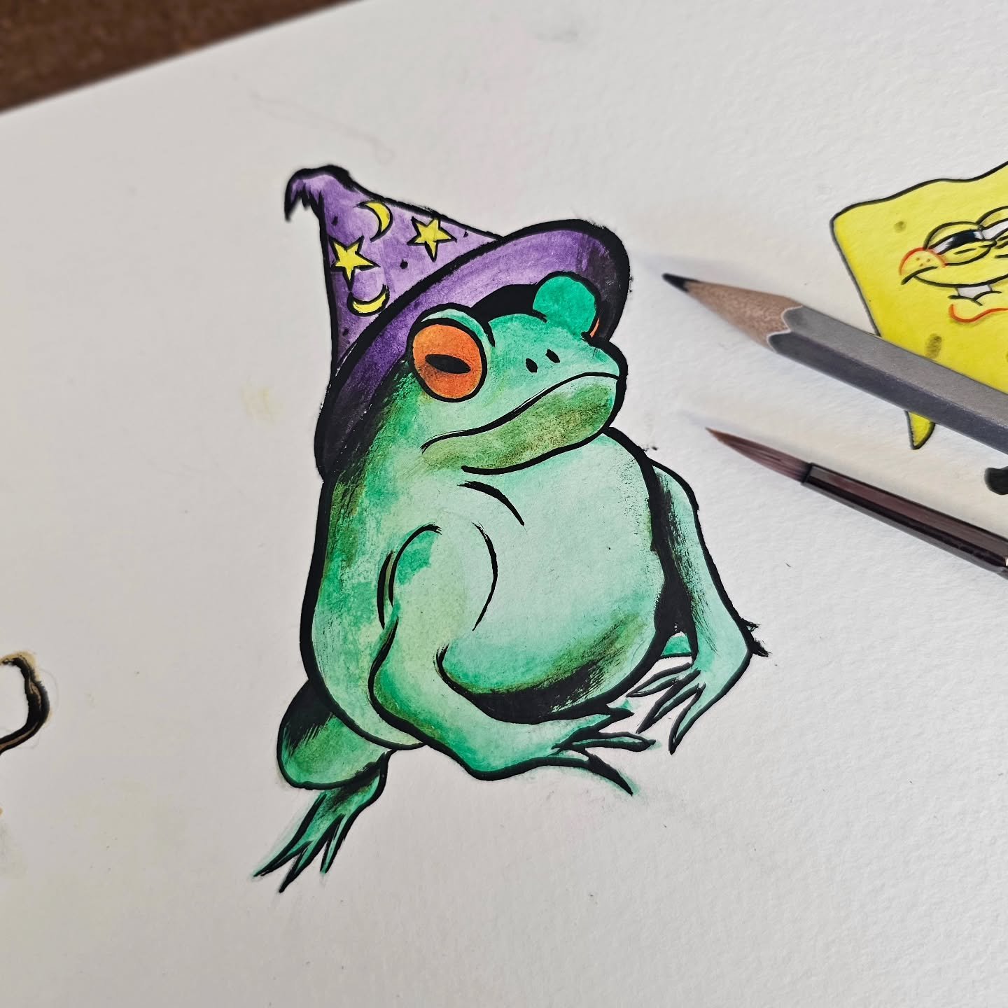 Colorful illustration of a frog wearing a purple wizard hat decorated with yellow stars and moons, with the frog standing upright on a white background.