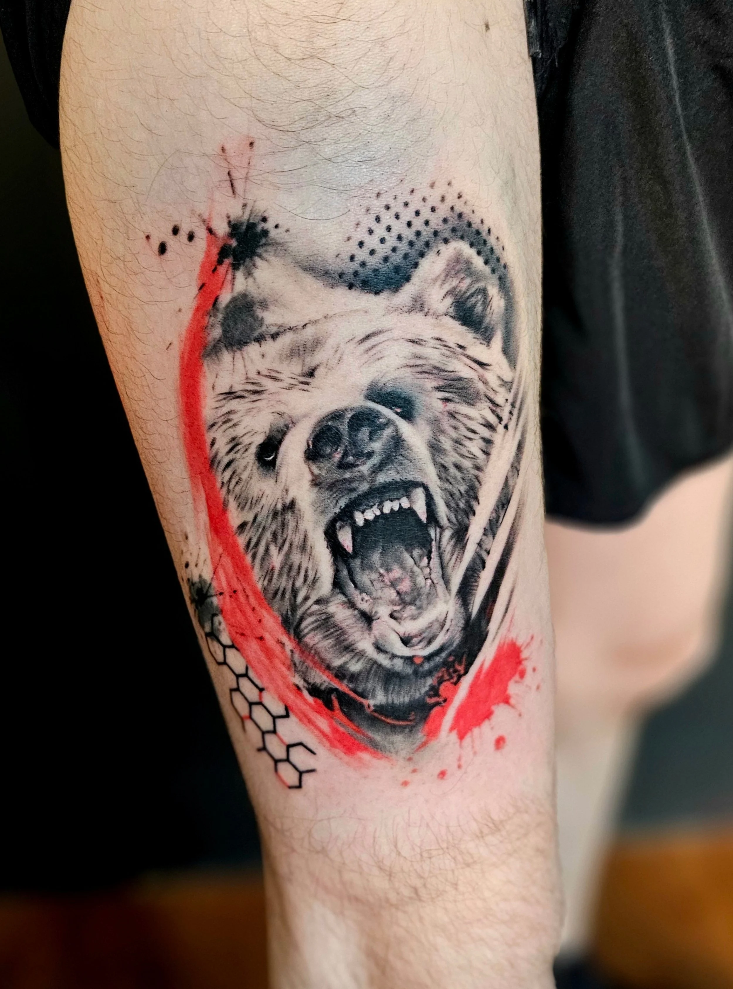 Tattoo of a snarling dog with detailed fur and open mouth, surrounded by black and red abstract elements and honeycomb patterns on a person's upper arm.
