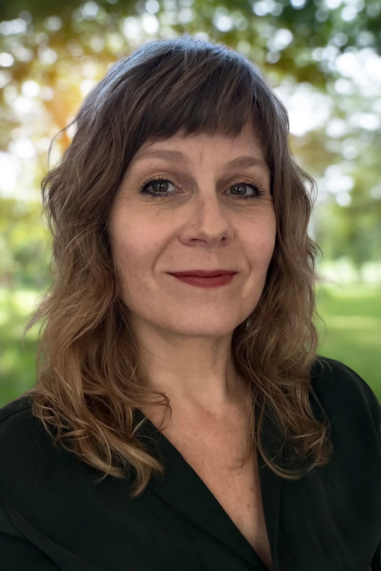 Portrait of a smiling woman with shoulder-length brown hair outdoors in a park