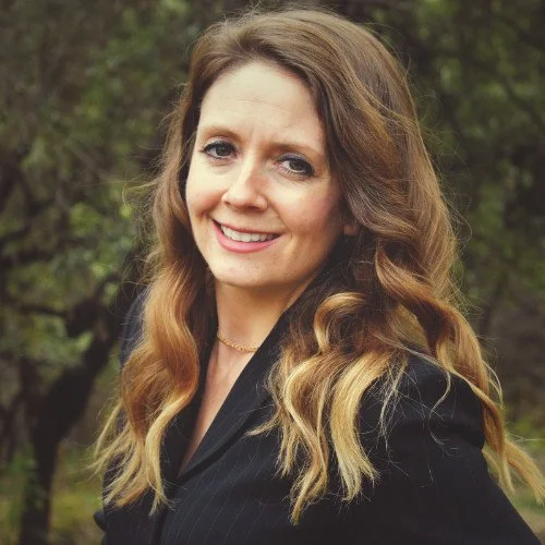 Smiling woman with long wavy brown hair wearing a black blazer outdoors