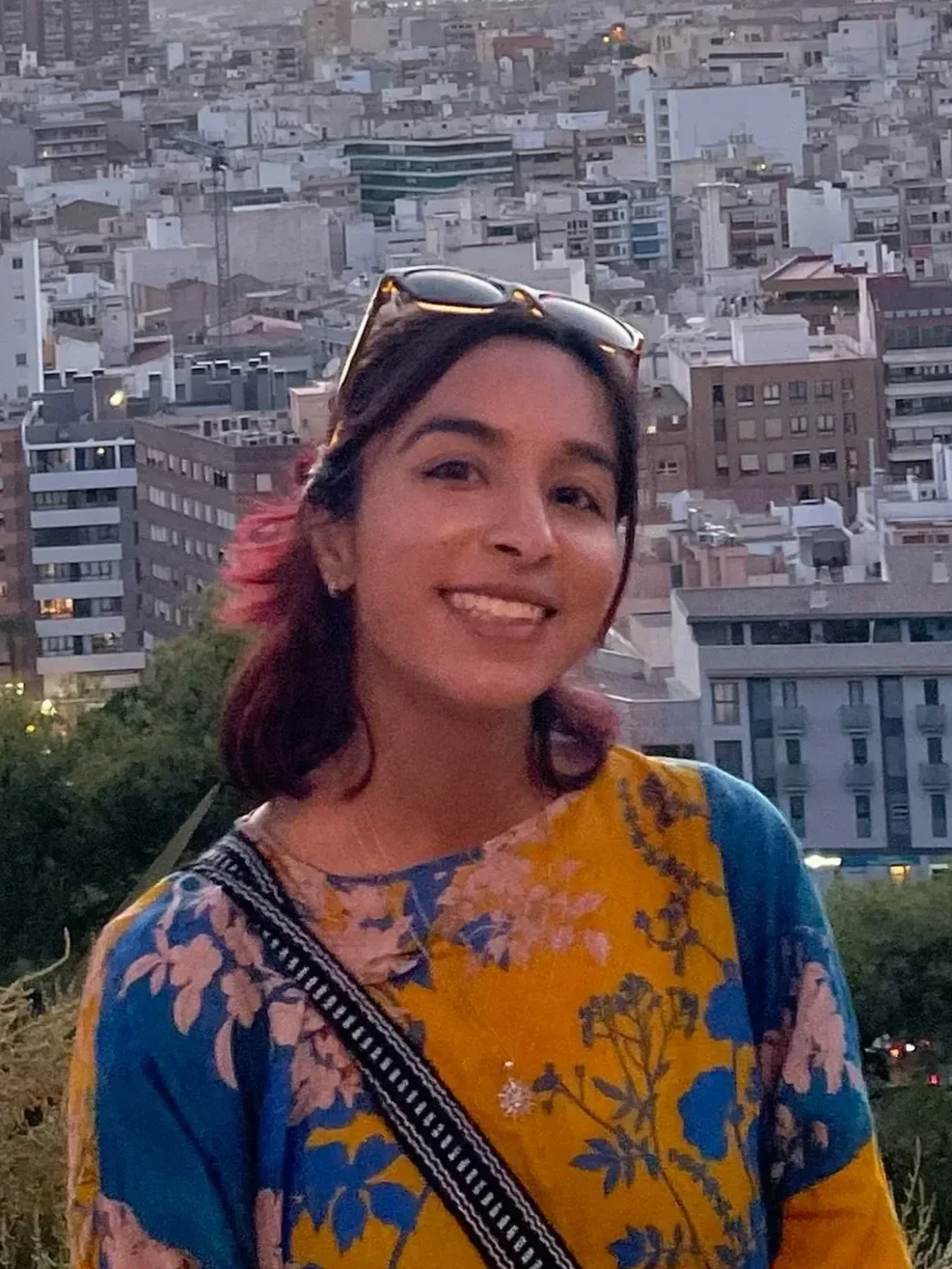 Smiling woman wearing sunglasses and a colorful floral top with a dense city skyline behind her