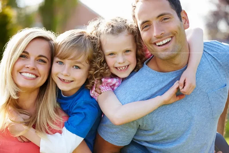 Parents and two children smiling together outdoors.