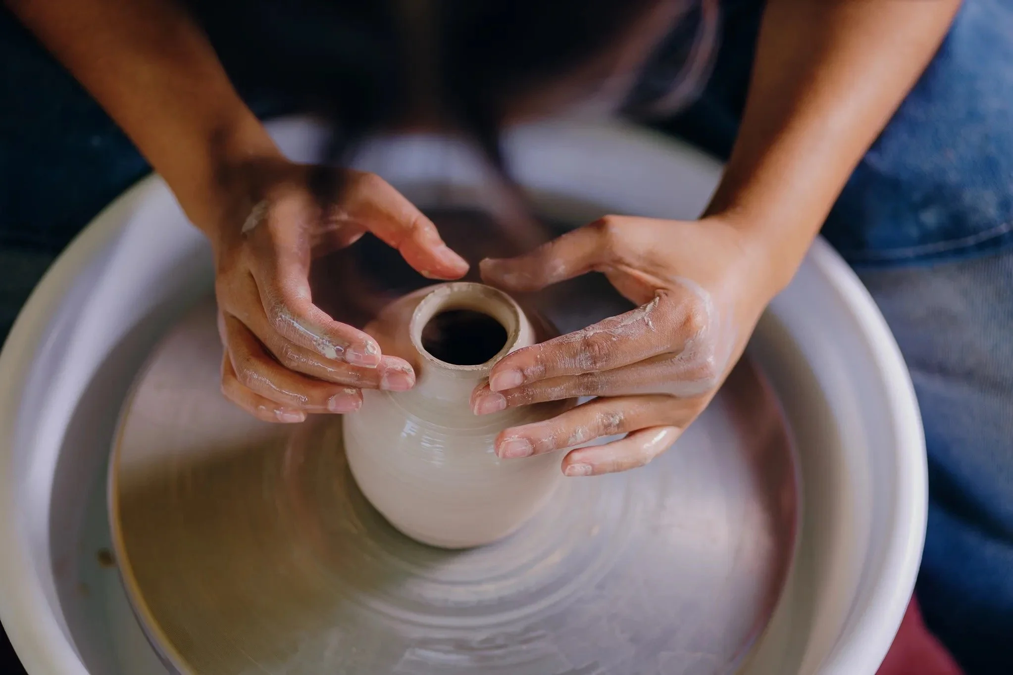 Hands shaping a clay vessel on a pottery wheel