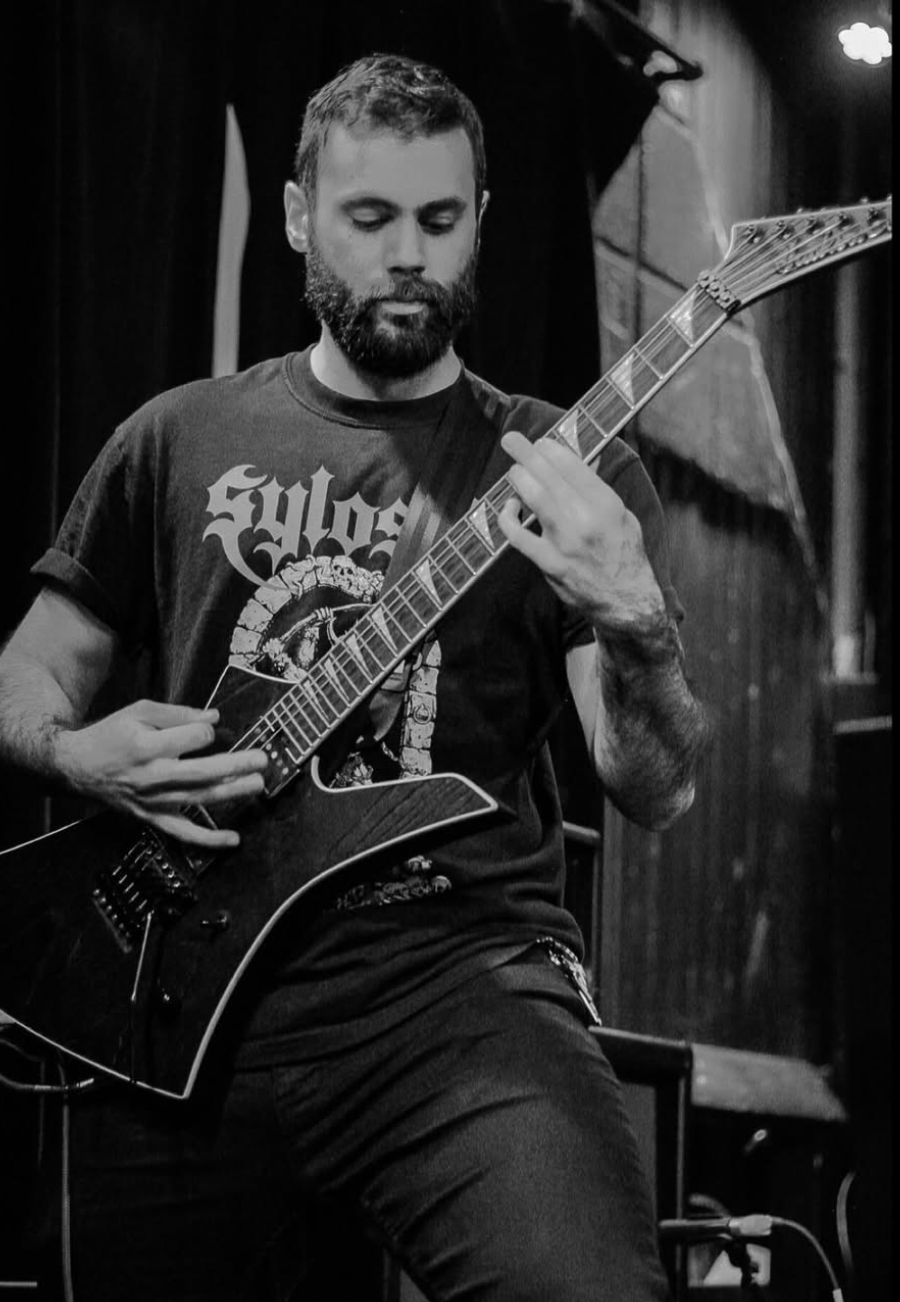 A man with a beard playing an electric guitar indoors