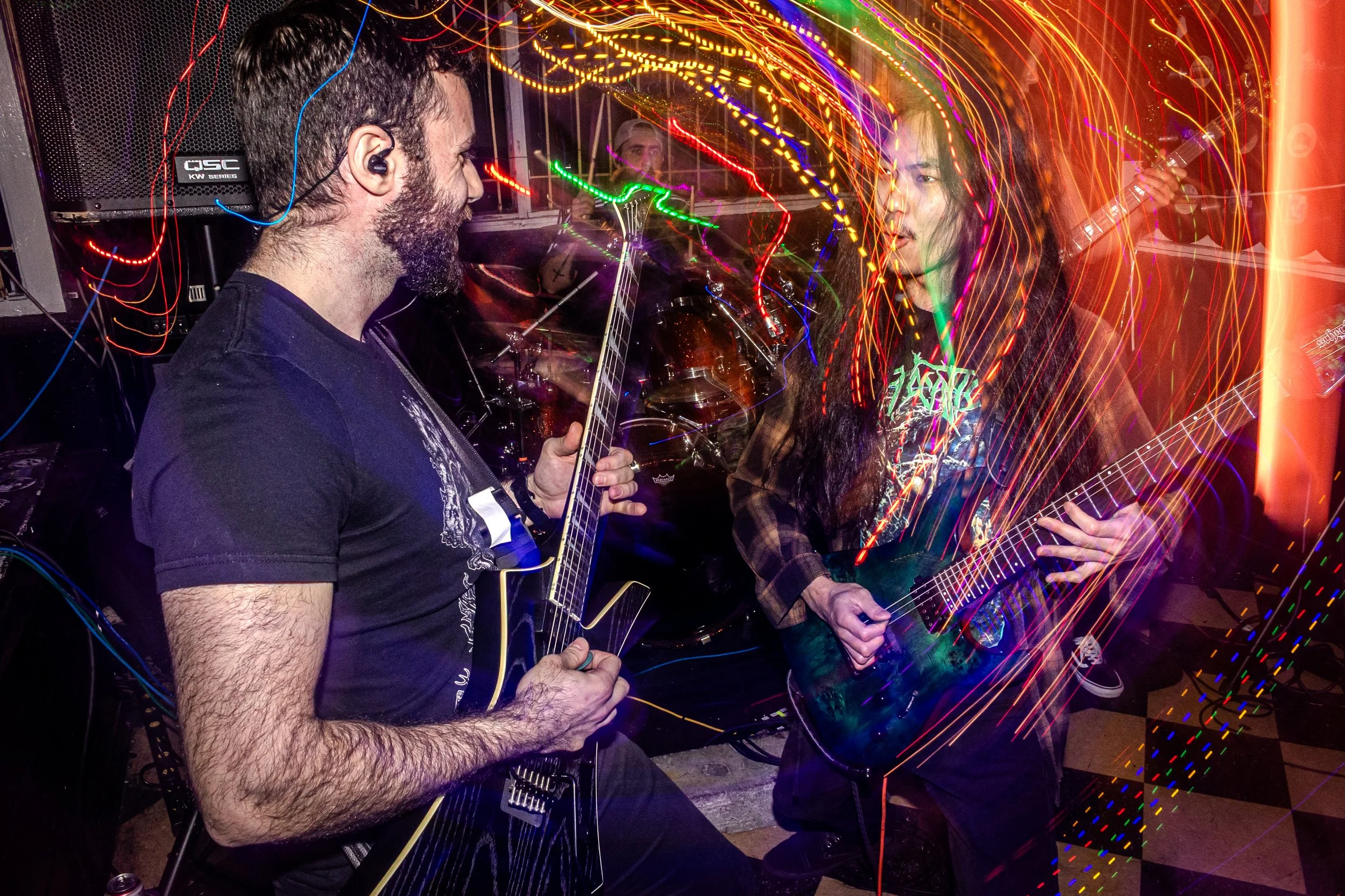 Two people, a man and a woman, playing guitars at a lively party with colorful light streaks and reflections surrounding them.