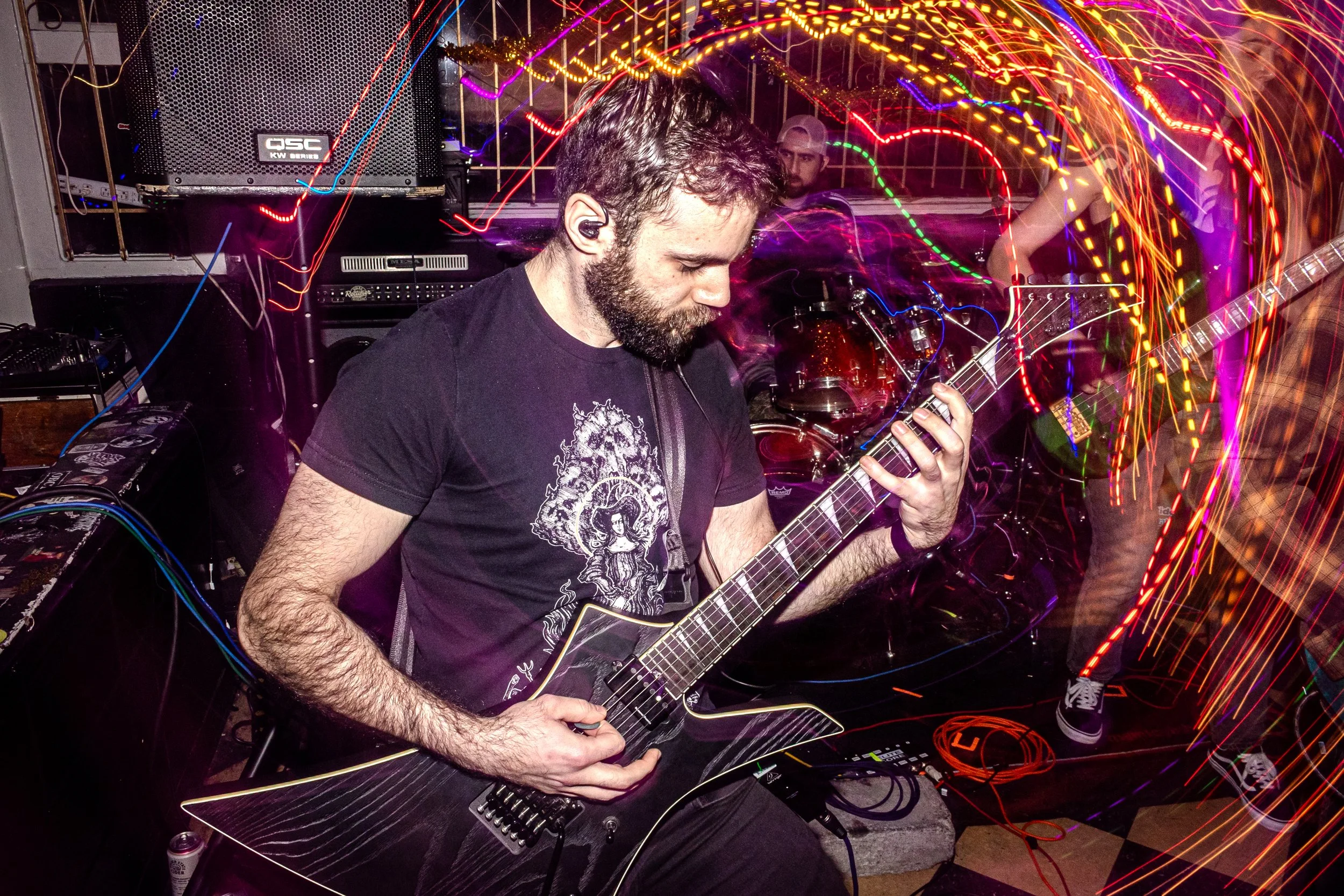 A man playing an electric guitar at a party or concert with colorful light streaks in the background.