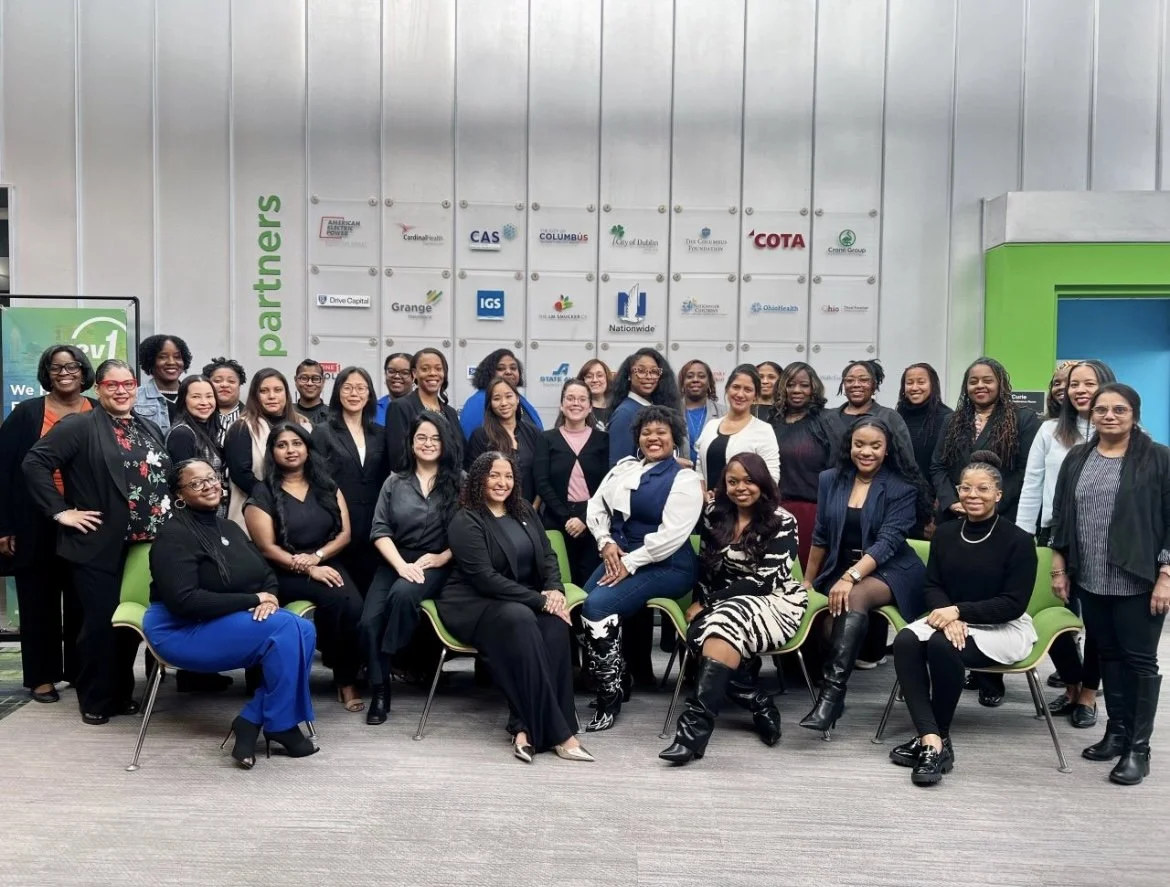 Group of professional women posing for a photo in a corporate office setting.