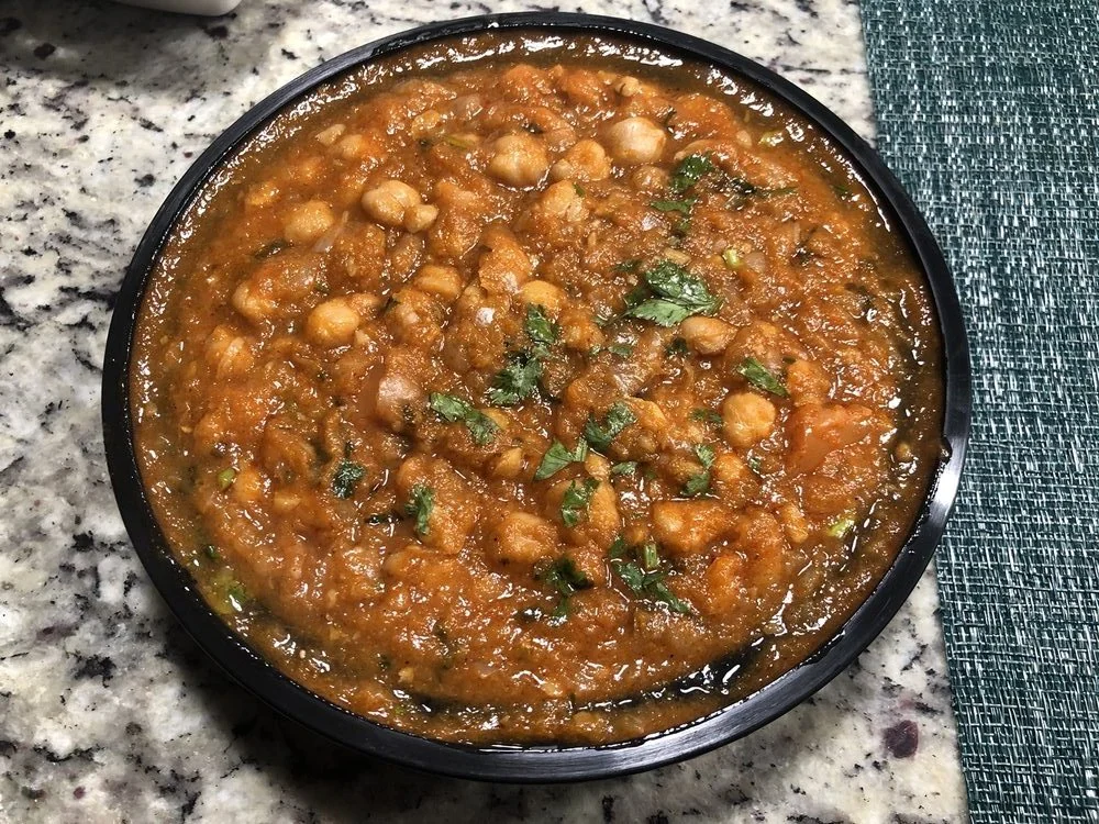 A bowl of chickpea curry garnished with chopped cilantro on a granite countertop.